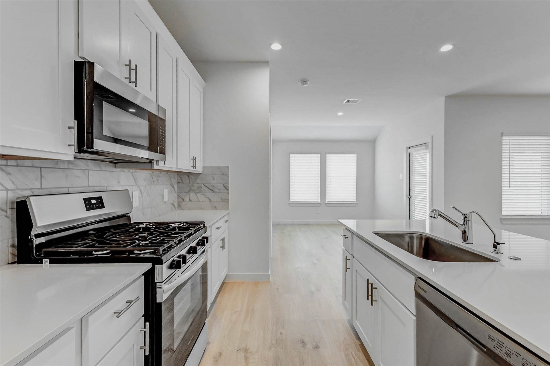 30307 Lighthouse Bluff Lane, Fulshear, TX 77441 This modern kitchen features sleek white cabinetry, stainless steel appliances, and a marble backsplash. It opens into a bright living area with large windows, offering a spacious and inviting atmosphere.