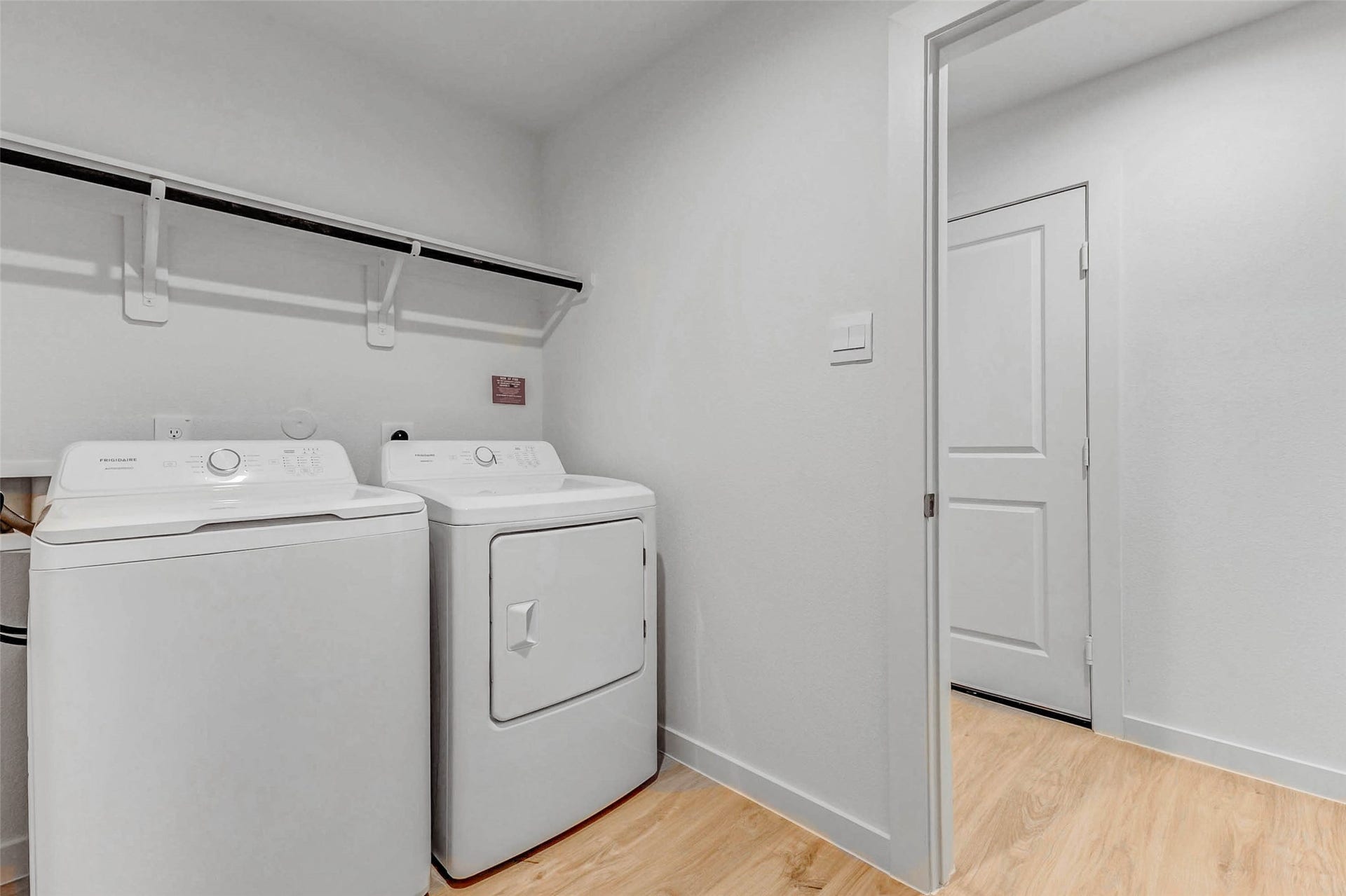 30307 Lighthouse Bluff Lane, Fulshear, TX 77441 Bright, functional laundry room with a provided washer and dryer, shelving for storage, and light wood flooring.