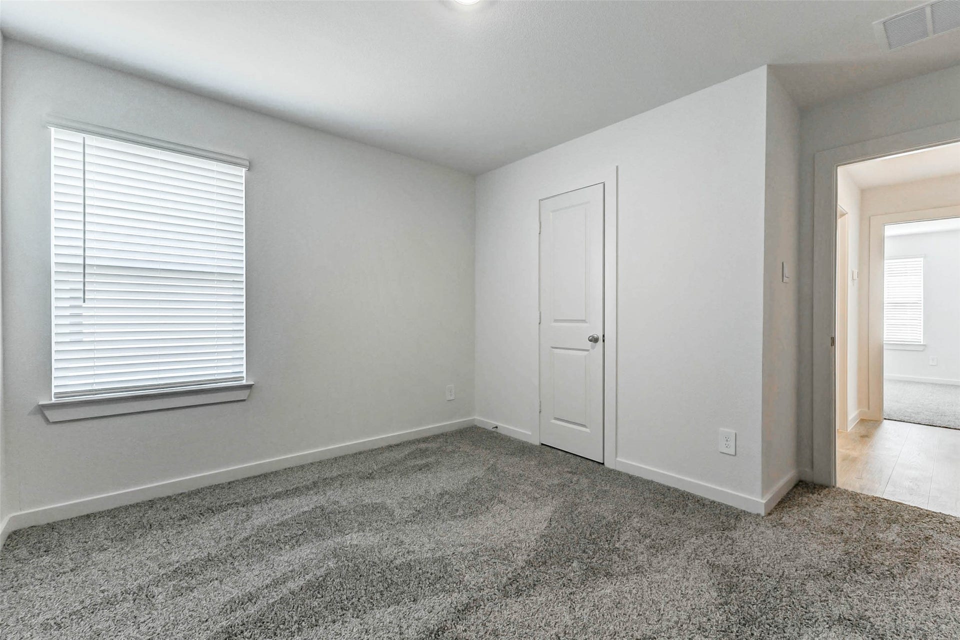 30307 Lighthouse Bluff Lane, Fulshear, TX 77441 This is a bright, carpeted room with neutral walls, featuring a window with blinds and a door leading to a hallway. Ideal for a bedroom or office space.