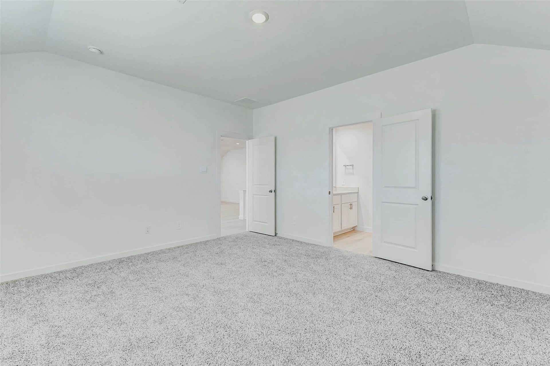 30307 Lighthouse Bluff Lane, Fulshear, TX 77441 This photo shows a bright, spacious bedroom with soft gray carpet and white walls. It features two doors, one leading to an adjoining bathroom with visible vanity, offering a clean and modern look.