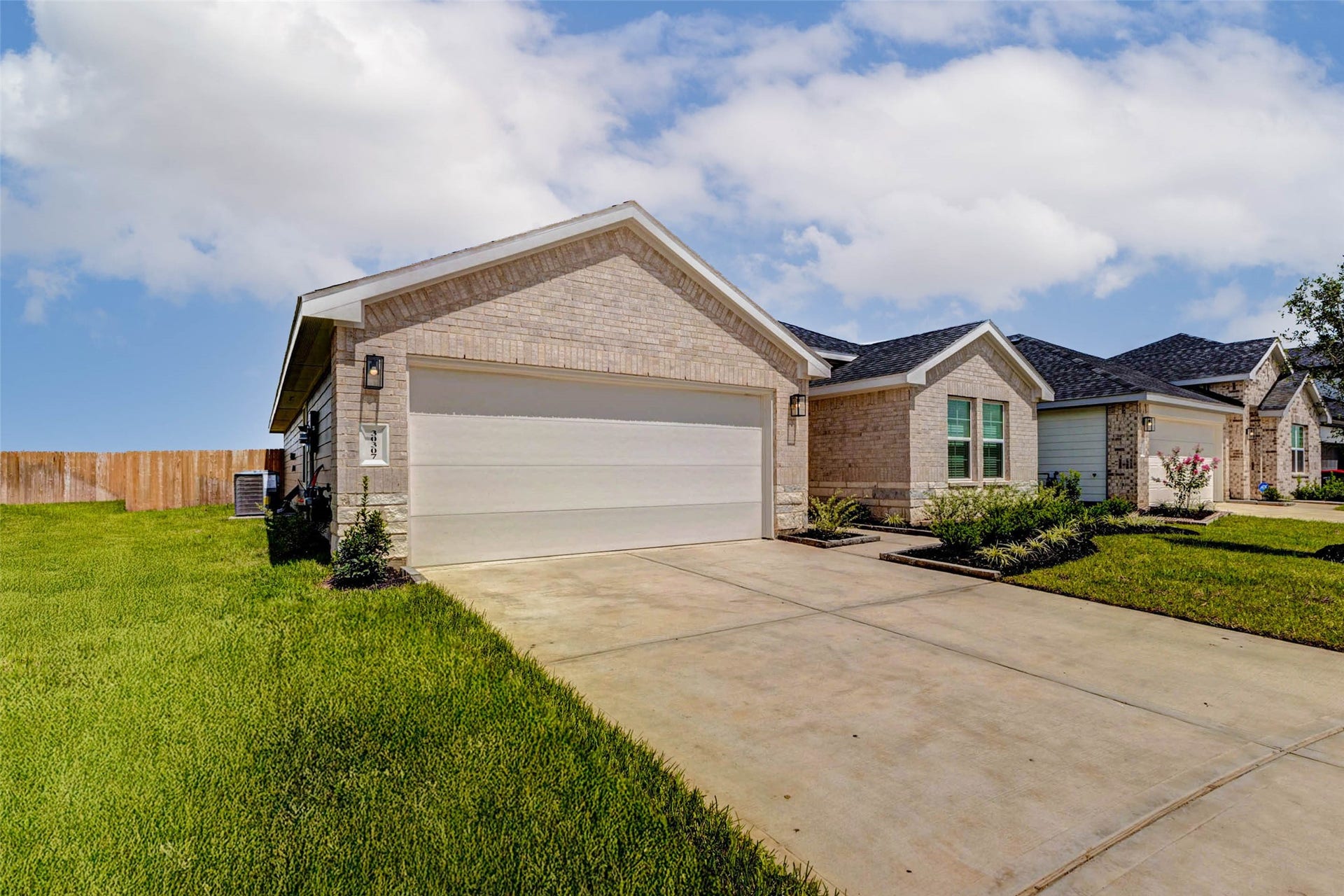 30307 Lighthouse Bluff Lane, Fulshear, TX 77441 Charming single-story home with a brick exterior and a neatly manicured lawn. The house features a spacious driveway leading to a two-car garage, surrounded by a well-maintained front yard and a wooden fence for added privacy.