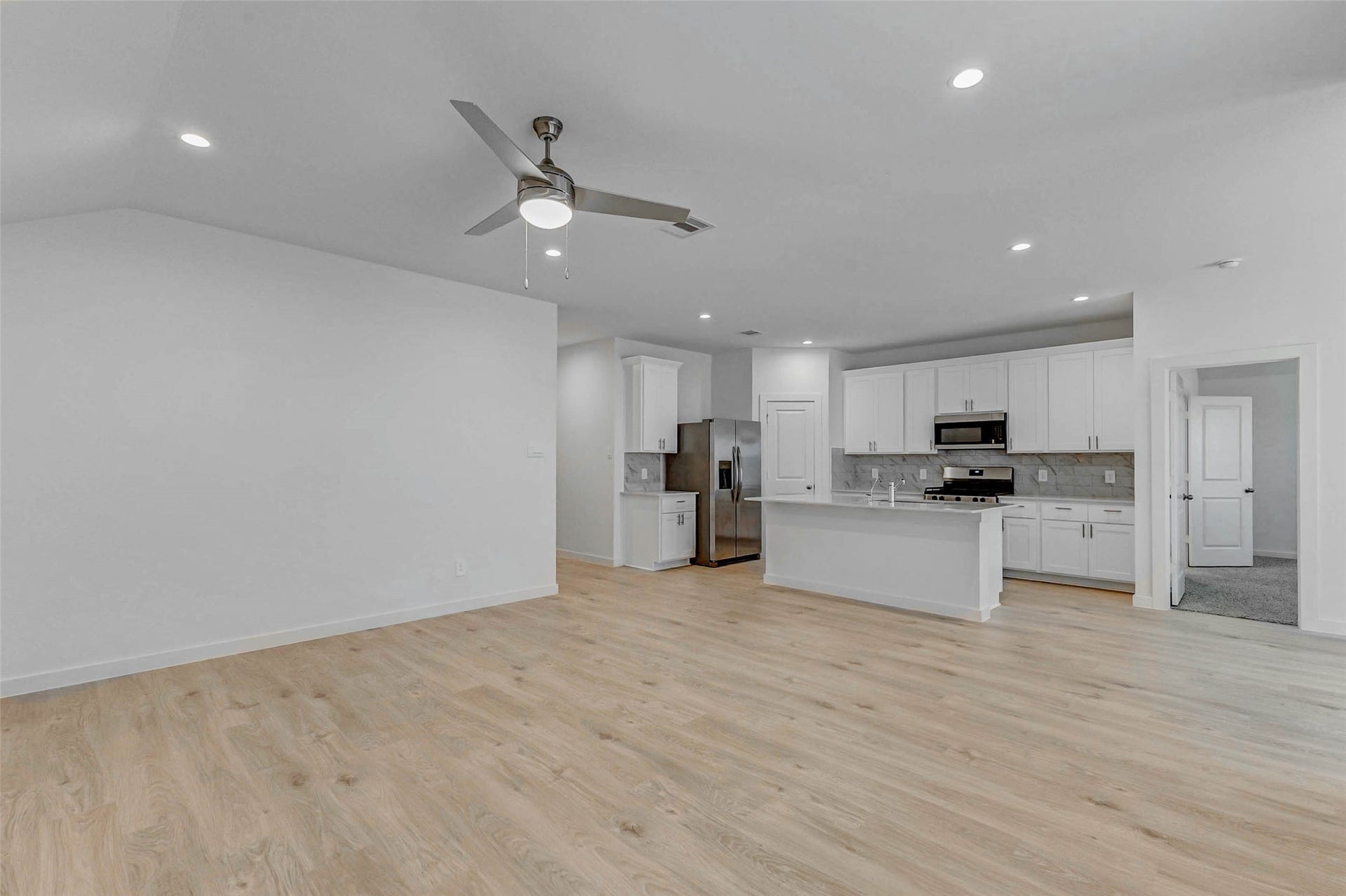 30307 Lighthouse Bluff Lane, Fulshear, TX 77441 This open-concept living space features light wood flooring, a modern kitchen with stainless steel appliances, white cabinetry, and a central island. The room is bright with recessed lighting and has a ceiling fan for comfort.