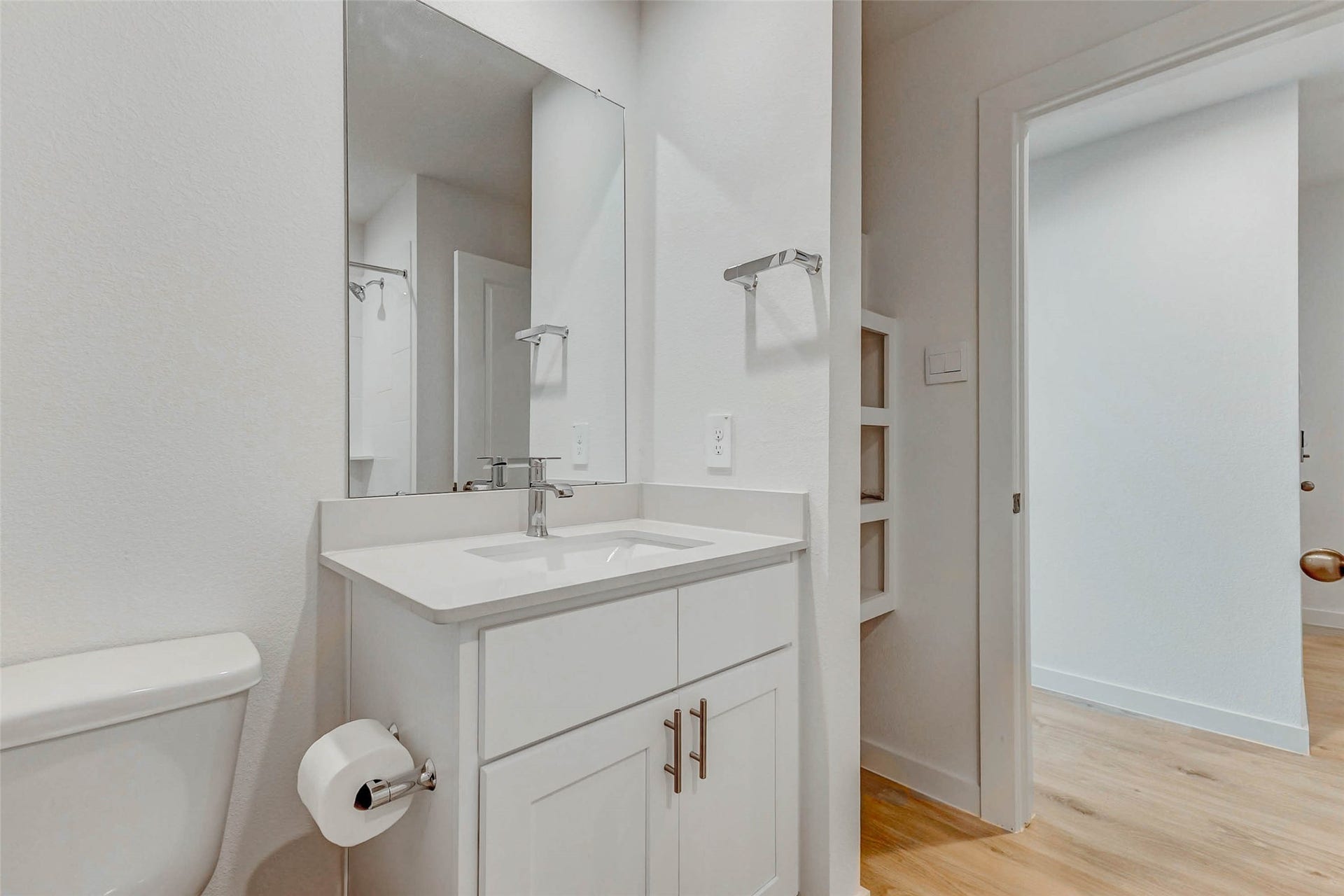 30307 Lighthouse Bluff Lane, Fulshear, TX 77441 Modern, bright bathroom with a sleek white vanity, a large mirror, and light wood flooring. The space is clean and minimalistic, offering built-in shelving and a fresh, airy feel.