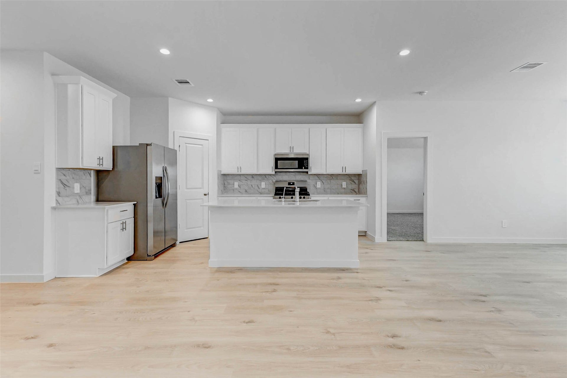 30307 Lighthouse Bluff Lane, Fulshear, TX 77441 Modern, open-concept kitchen with white cabinetry, stainless steel appliances, and a central island. The space is bright with light wood flooring, providing a clean and inviting atmosphere.