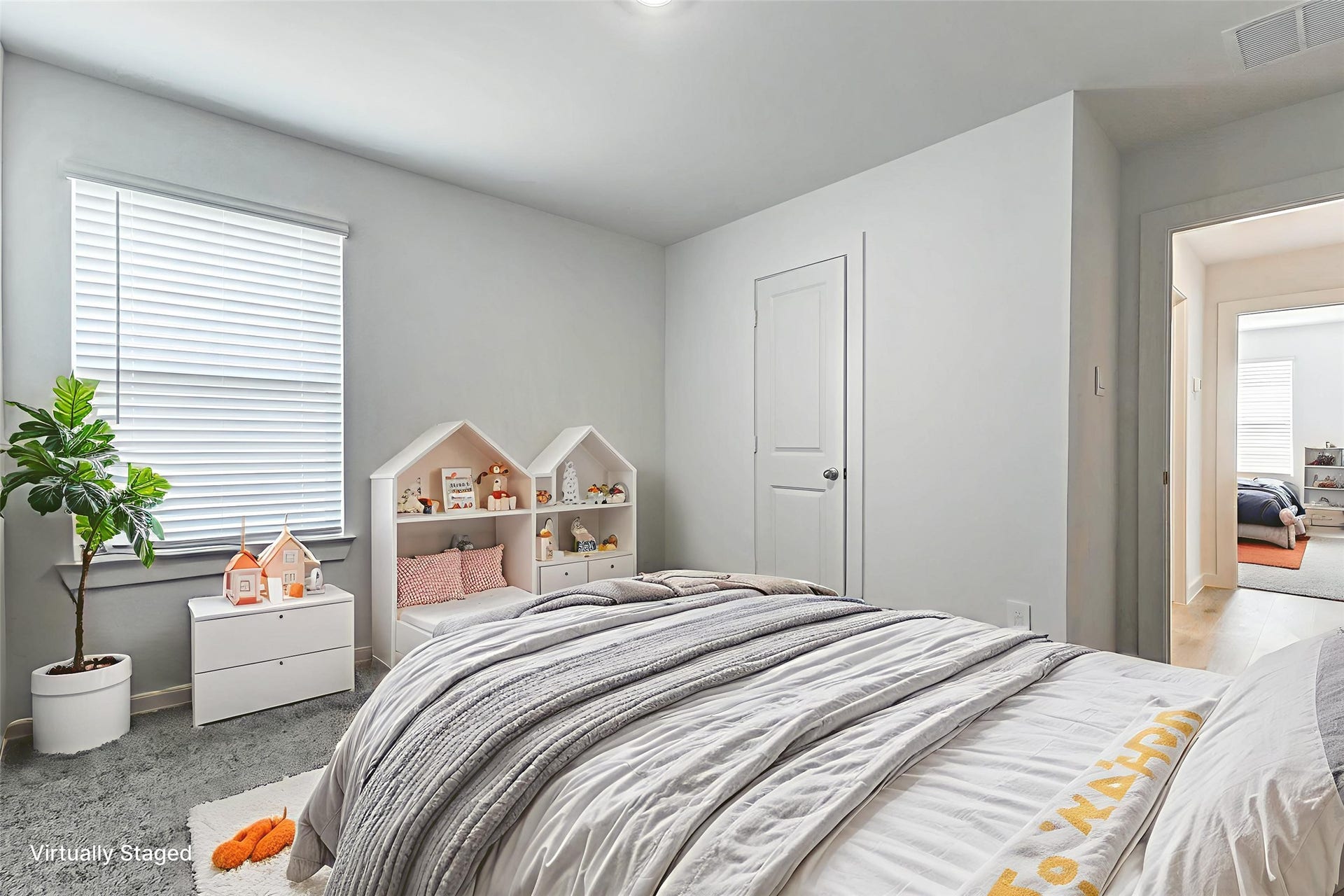 30307 Lighthouse Bluff Lane, Fulshear, TX 77441 This is a virtually staged bedroom with soft gray walls and carpet. It features a cozy bed, house-shaped shelves with decor, a small chest of drawers, and a potted plant. A door leads to an adjacent room, enhancing the space's connectivity.