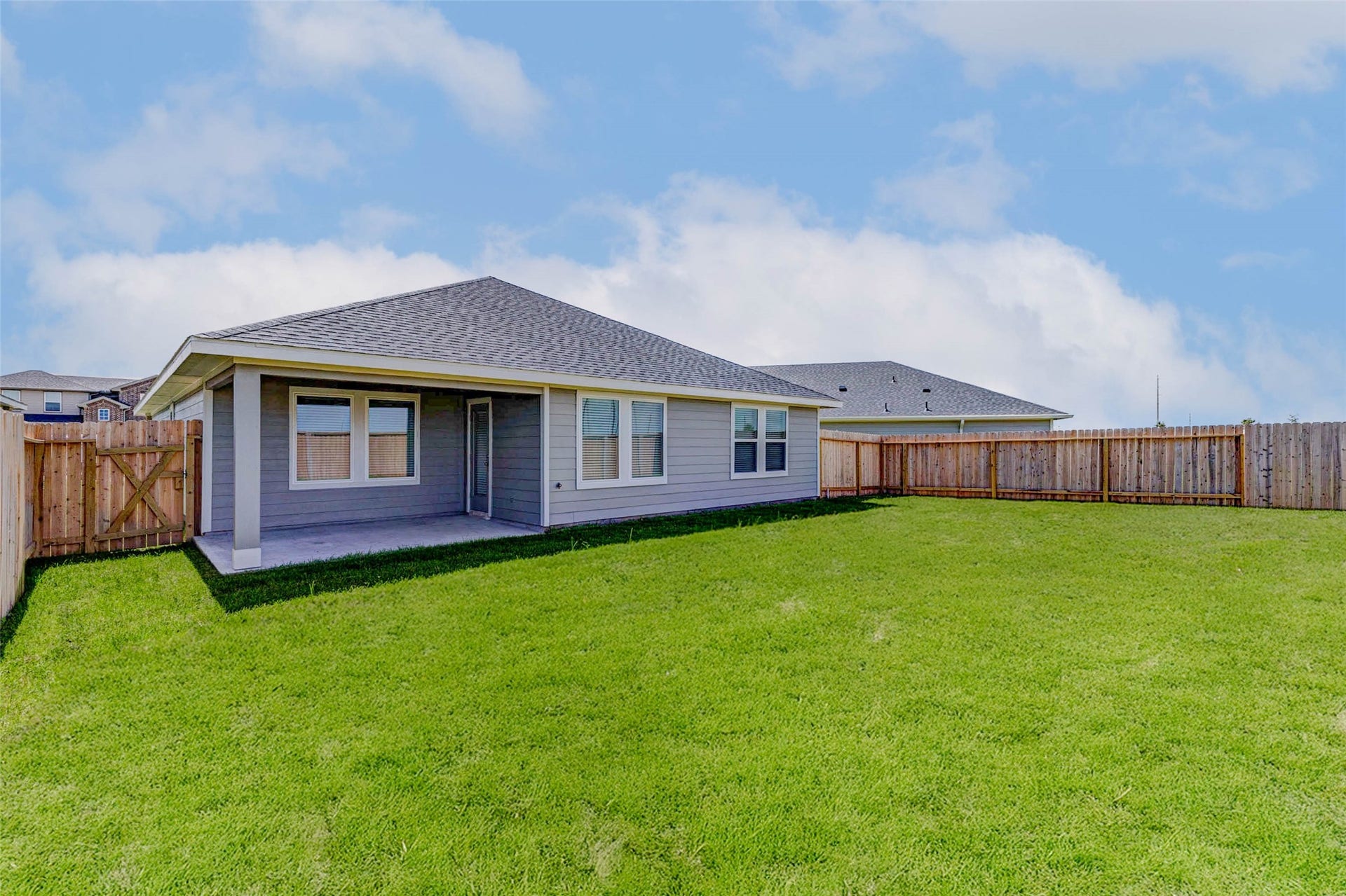 30307 Lighthouse Bluff Lane, Fulshear, TX 77441 Single-story house with a spacious, fenced backyard. The exterior is modern with a covered patio area, perfect for outdoor activities. The lawn is well-maintained, offering plenty of space for gardening or recreation.