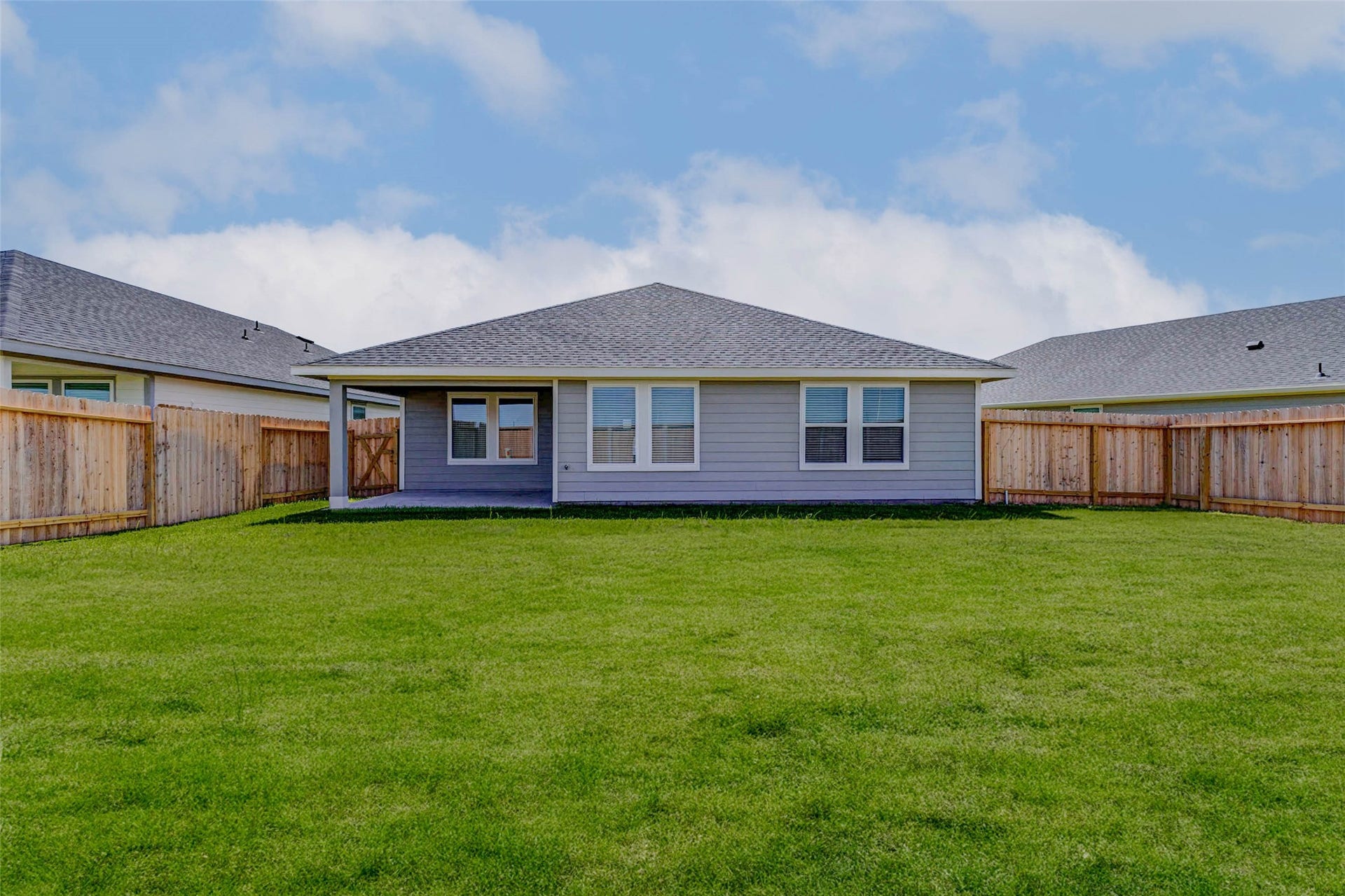 30307 Lighthouse Bluff Lane, Fulshear, TX 77441 Back view of a single-story home with a spacious, well-maintained lawn and wooden fencing for privacy. The house has large windows and a covered patio area, ideal for outdoor activities.