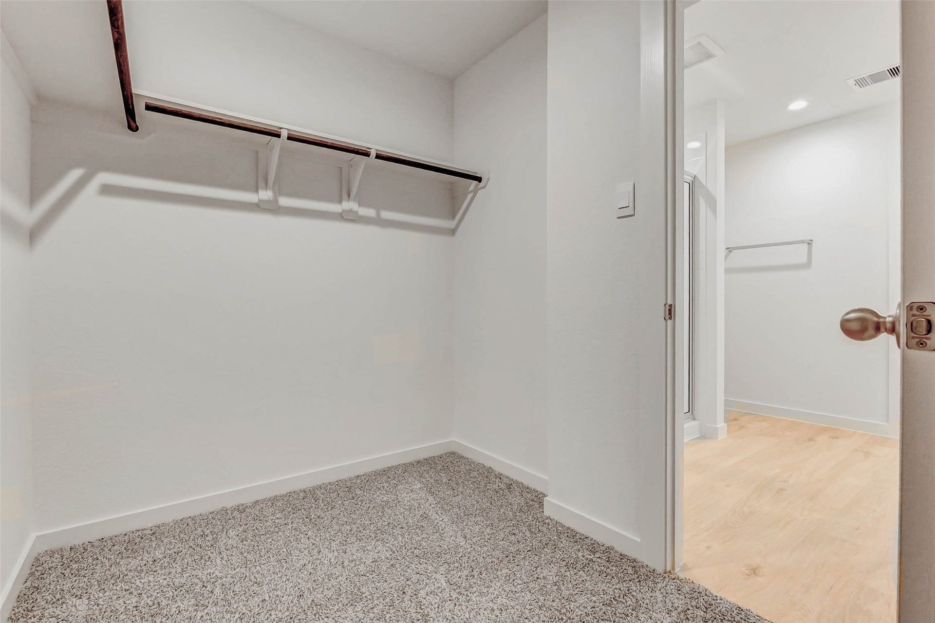 30307 Lighthouse Bluff Lane, Fulshear, TX 77441 Spacious walk-in closet with carpeted flooring and a wooden hanging rod. It opens into a well-lit adjoining room with light wood flooring.