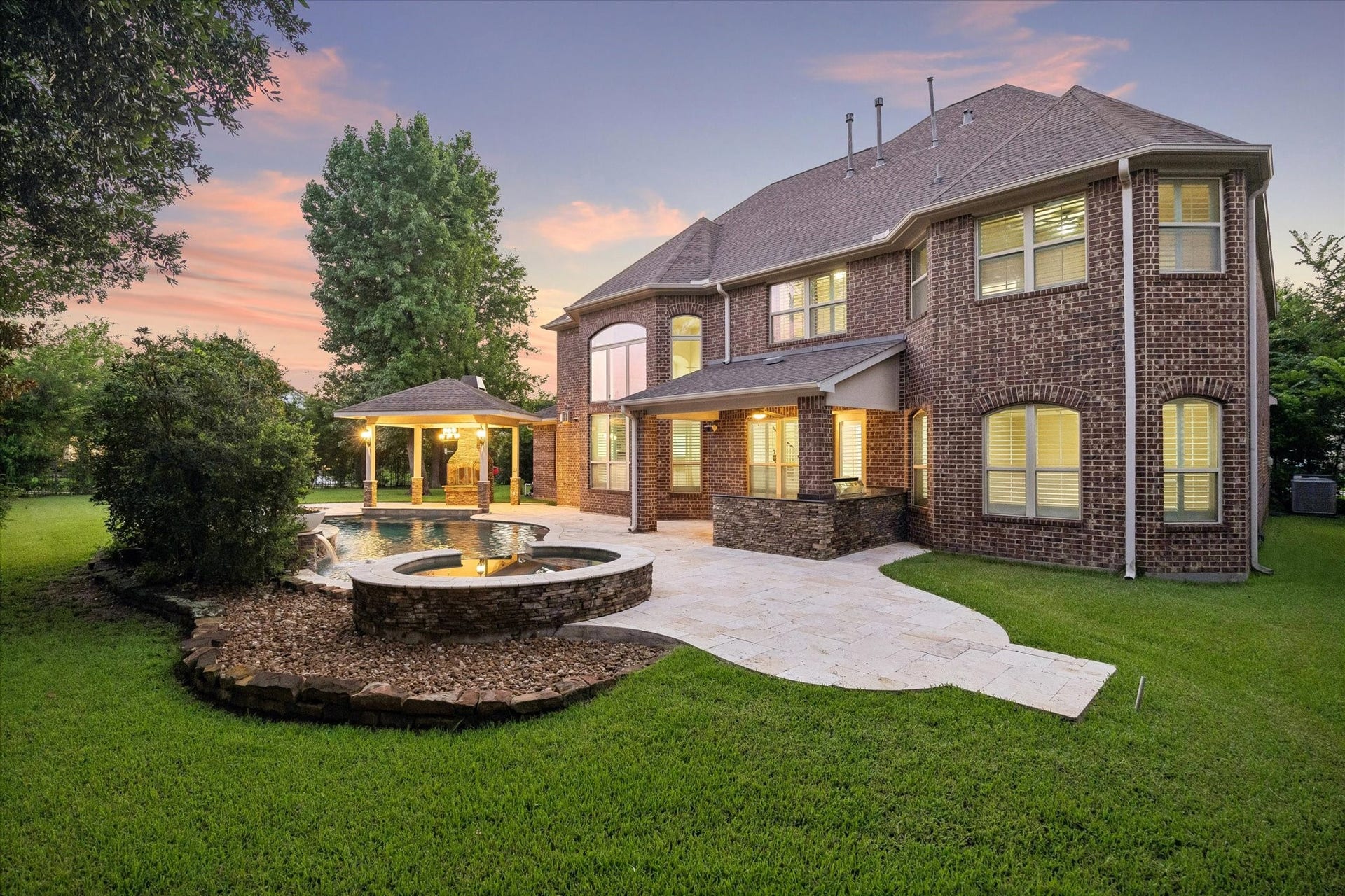 A stunning perspective of this exceptional outdoor oasis, featuring a resort-style pool and spa, expansive travertine decking, outdoor kitchen, and thoughtfully designed gathering spaces, creating the perfect setting for both elegant entertaining and everyday enjoyment.