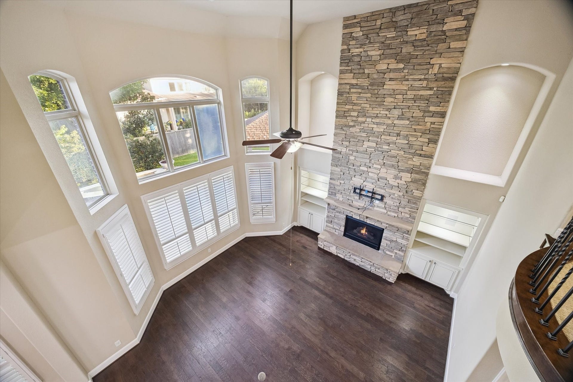A breathtaking perspective from the upper-level iron-railed balcony reveals the grandeur of the family room, where soaring ceilings, a striking floor-to-ceiling stone fireplace, and expansive windows create a bright and inviting atmosphere.