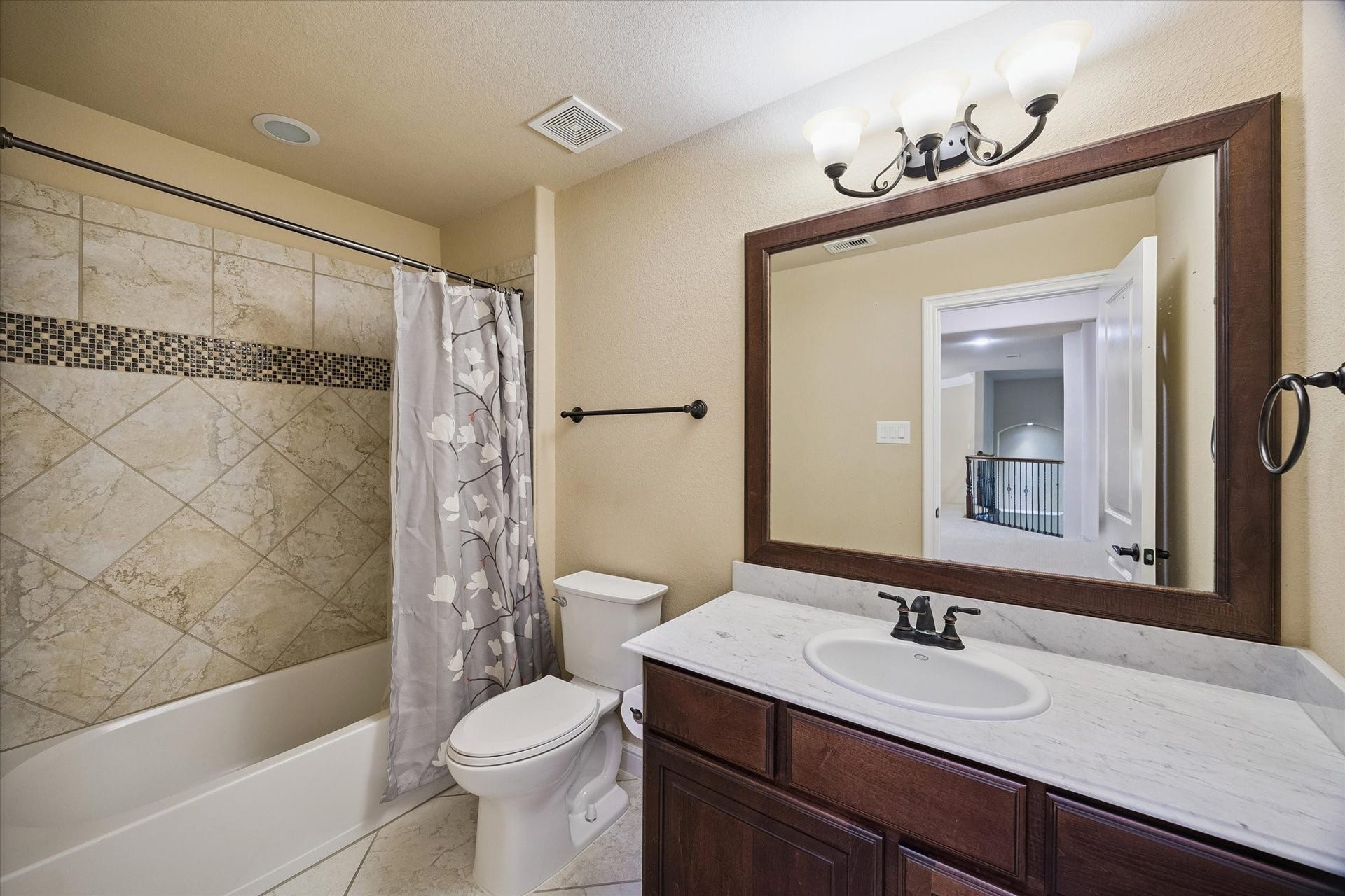 A well-appointed secondary bathroom conveniently located off the upstairs landing. Featuring a spacious vanity with marble-look countertops, elegant framed mirror, and a tub/shower combination accented with decorative tile work, this bathroom comfortably serves family members and guests alike.