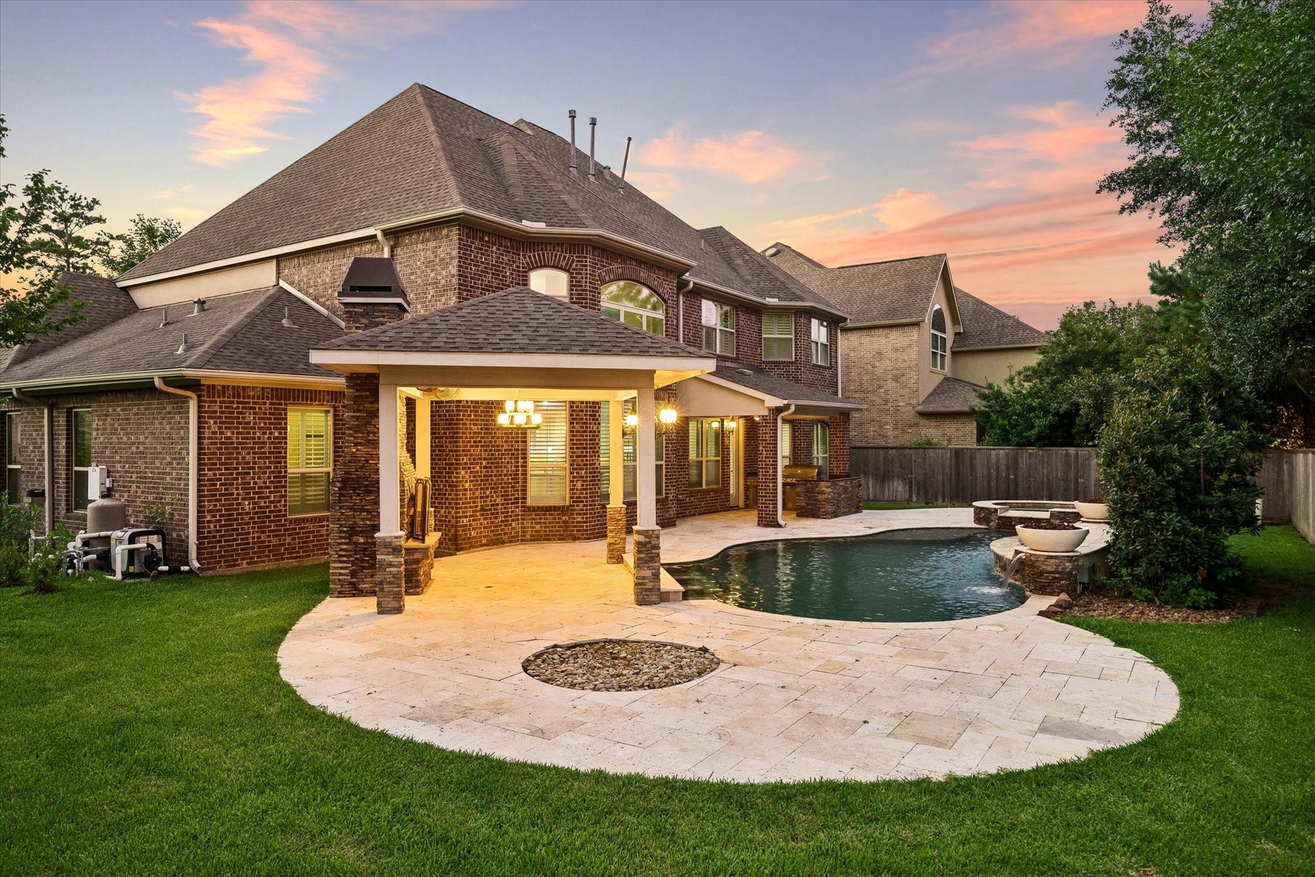 This beautifully designed outdoor living space offers a resort-style pool and spa, outdoor kitchen, expansive travertine decking, and a separate covered patio with fireplace, an inviting setting for entertaining or enjoying quiet evenings under the Texas sky.