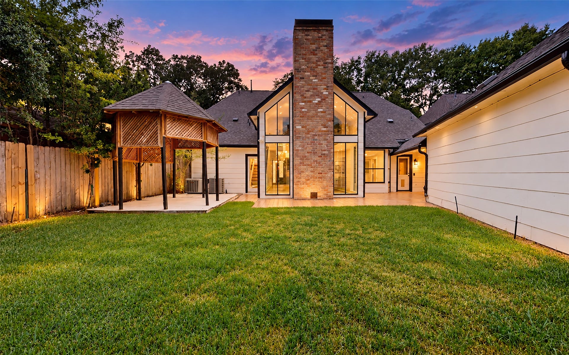 1407 Sherfield Ridge Drive, Katy, TX 77450 1407 Sherfield Ridge Dr, Spacious, beautifully landscaped backyard featuring lush green lawn, mature trees, a privacy fence, and a charming covered gazebo. The homes dramatic floor-to-ceiling windows and striking brick fireplace create an impressive architectural backdrop, while exterior lighting adds warmth and ambianceperfect for relaxing or entertaining outdoors.