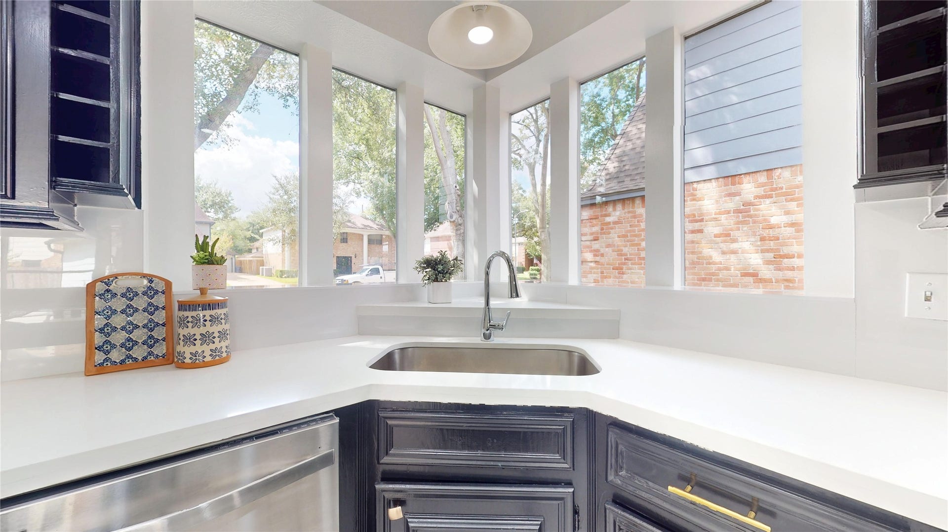 1407 Sherfield Ridge Drive, Katy, TX 77450 1407 Sherfield Ridge Dr, Bright kitchen with white countertops, dark cabinetry and an under-mount sink with a modern gooseneck faucet. A beautiful wraparound wall of large windows fills the space with abundant natural light and offers peaceful views of the mature trees and surrounding greenery.