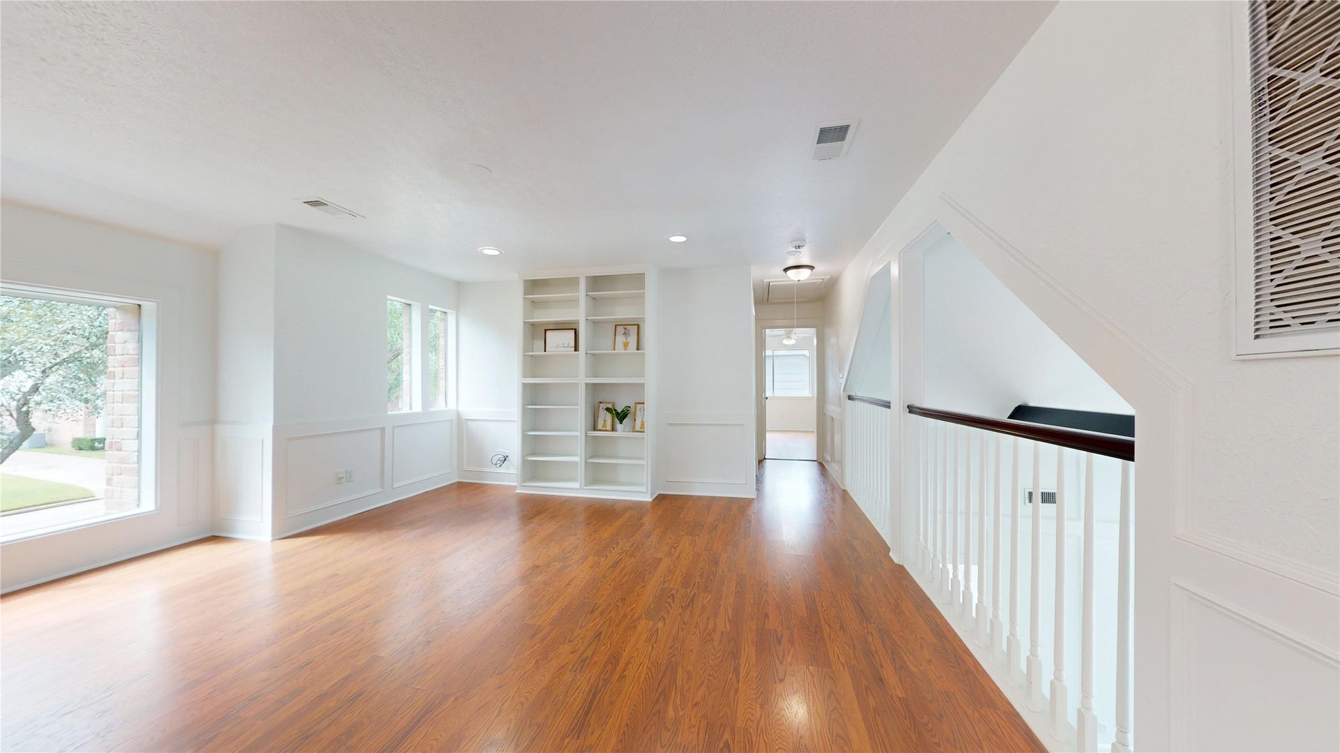 1407 Sherfield Ridge Drive, Katy, TX 77450 1407 Sherfield Ridge Dr, Bright and spacious upstairs living area featuring warm wood flooring, recessed lighting, built-in shelving, and abundant natural light from multiple windows. Decorative wall molding adds character, while the open railing overlooks the lower level. The versatile space is ideal for a game room, media area, home office, or additional family room.