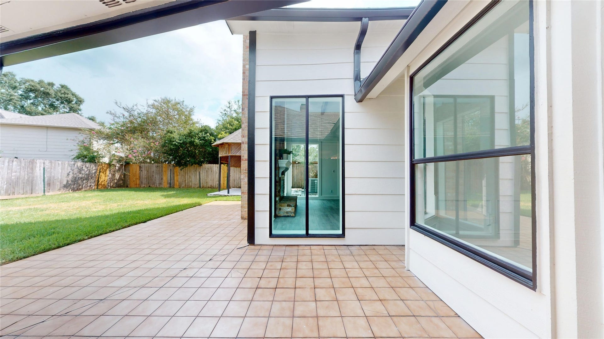 1407 Sherfield Ridge Drive, Katy, TX 77450 1407 Sherfield Ridge Dr, Spacious covered back patio featuring a tiled surface, modern black trim, and large windows overlooking the backyard. The extended patio provides plenty of room for outdoor seating and entertaining, with easy access to the large, fully fenced backyard and mature landscaping.