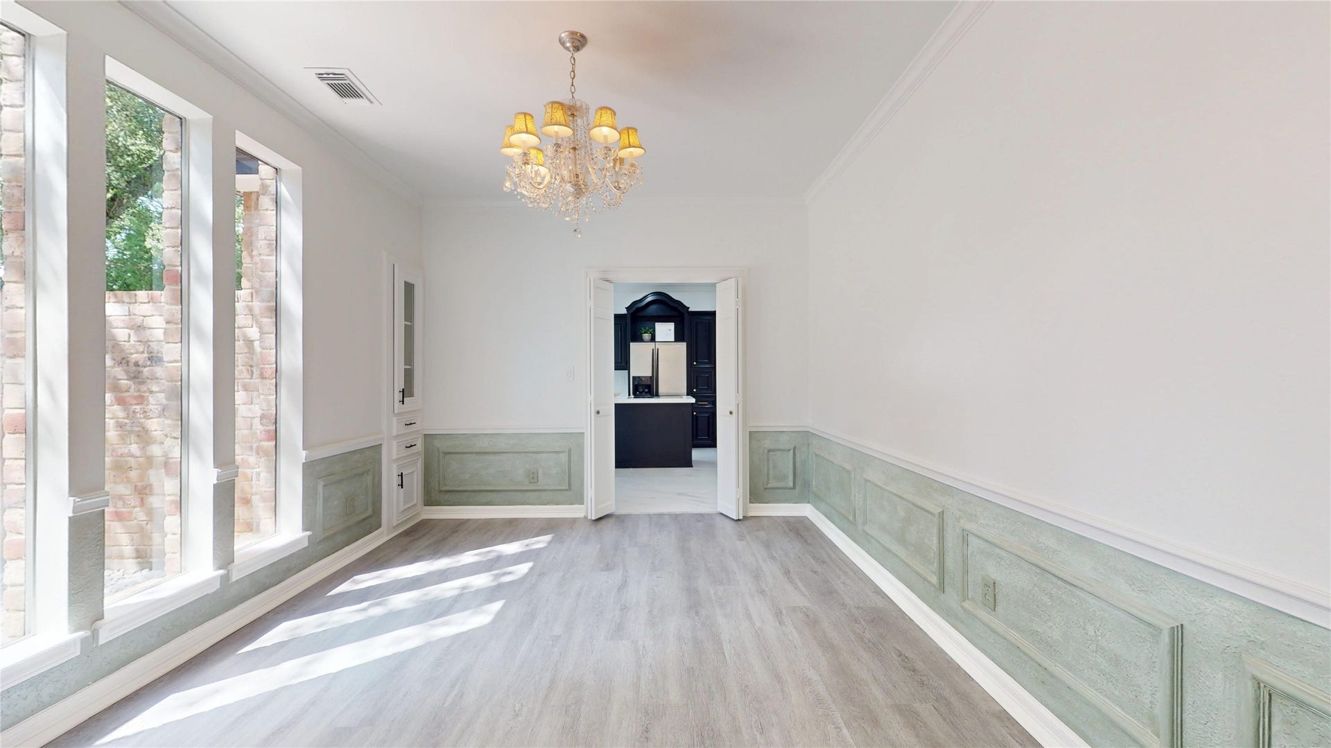 1407 Sherfield Ridge Drive, Katy, TX 77450 1407 Sherfield Ridge Dr, Formal dining area featuring decorative soft sage wainscoting/picture frame wall molding, tall windows, accented by a crystal chandelier and built in cabinetry and wooden laminate florring throughout with entranceway to the kitchen.