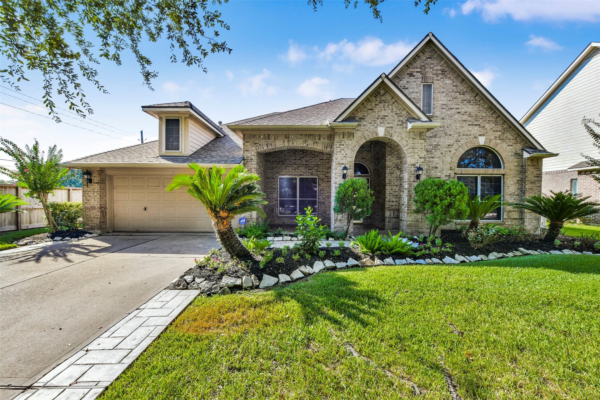 9902 Autumn Lake Trail, Pearland, TX 77584 Charming brick home with elegant arched entryway, lush landscaping, and a spacious oversized garage.