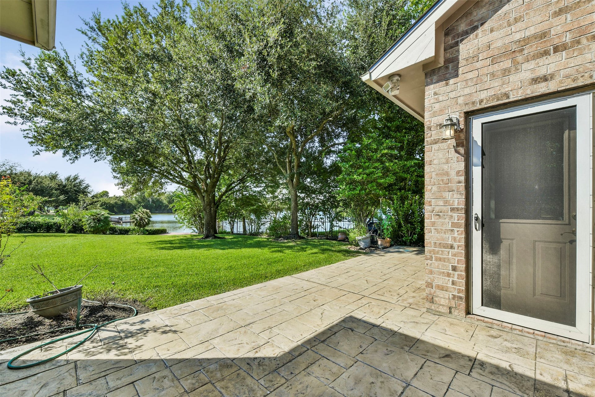 9902 Autumn Lake Trail, Pearland, TX 77584 Charming backyard with a spacious patio, lush green lawn, and serene lake views framed by mature trees, perfect for outdoor relaxation.