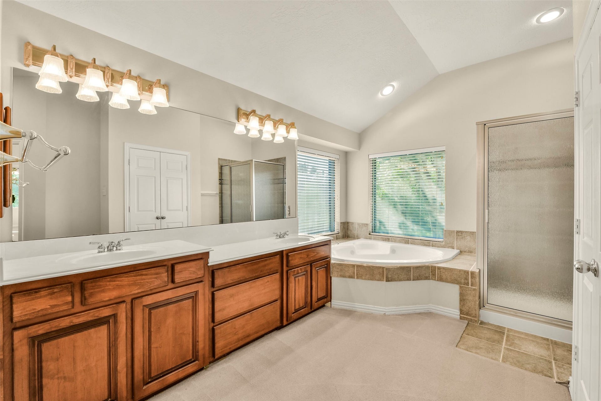 9902 Autumn Lake Trail, Pearland, TX 77584 Spacious bathroom with dual sinks, elegant wood cabinetry, a luxurious soaking tub, and a separate glass-enclosed shower, all bathed in natural light from large windows.
