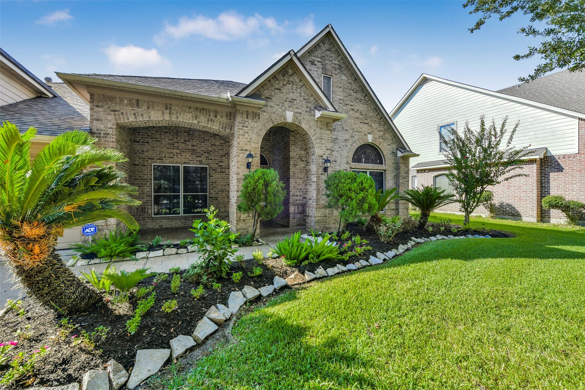 9902 Autumn Lake Trail, Pearland, TX 77584 Charming brick exterior with elegant archways, lush landscaping, and a well-maintained lawn create inviting curb appeal.