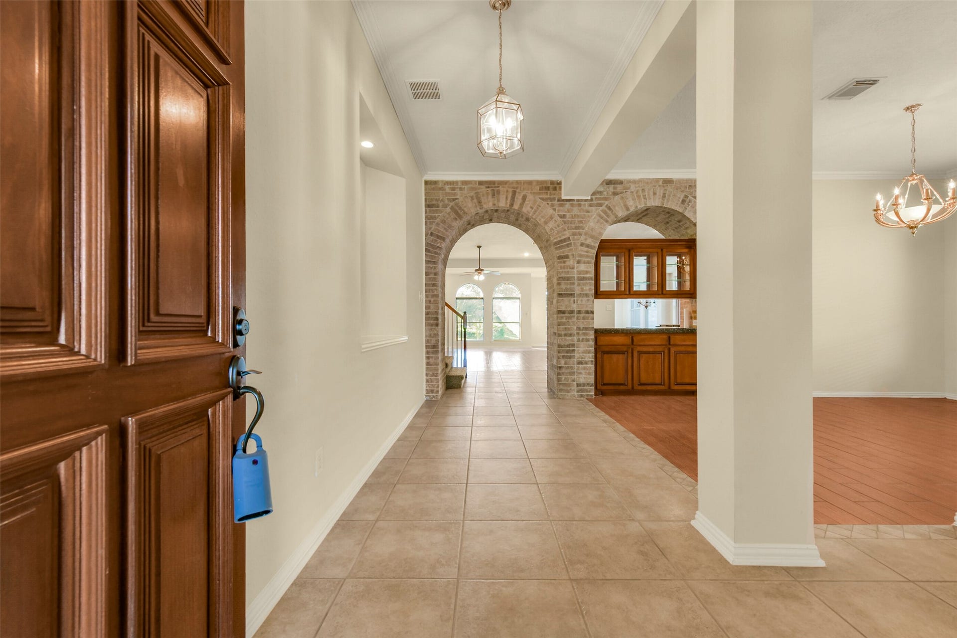 9902 Autumn Lake Trail, Pearland, TX 77584 Step into a welcoming foyer featuring elegant tile flooring, leading to a spacious living area accentuated by charming brick arches and a built-in cabinet, with stylish light fixtures enhancing the warm ambiance.