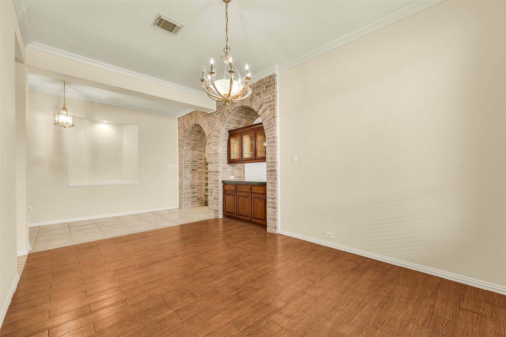 9902 Autumn Lake Trail, Pearland, TX 77584 Elegant dining area with warm wood flooring and a stylish chandelier, complemented by a charming brick archway leading to a built-in cabinet and wet bar.