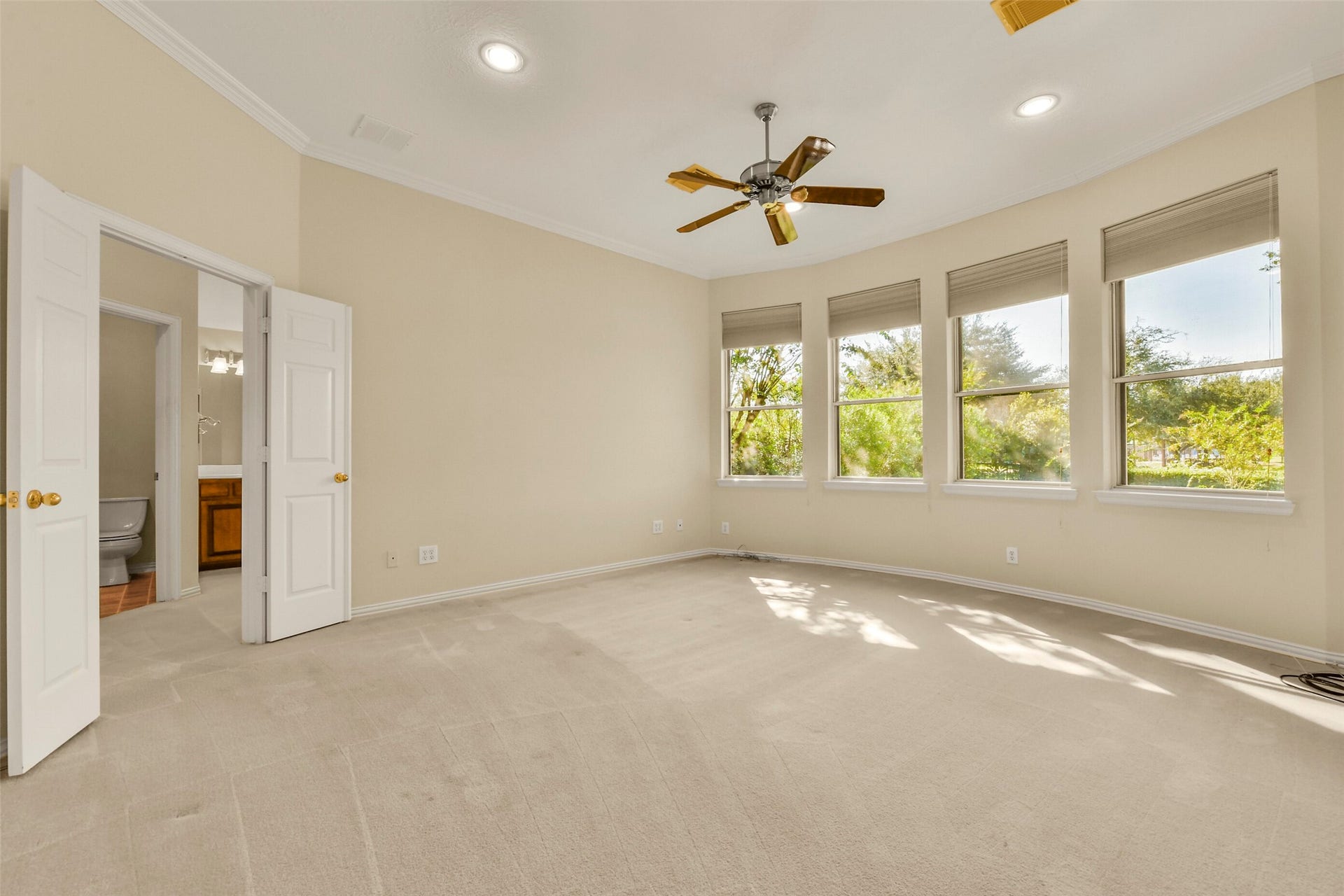 9902 Autumn Lake Trail, Pearland, TX 77584 Bright and spacious primary bedroom with large windows offering abundant natural light, neutral walls, and a ceiling fan. Access to an ensuite bathroom through double doors enhances convenience and comfort.