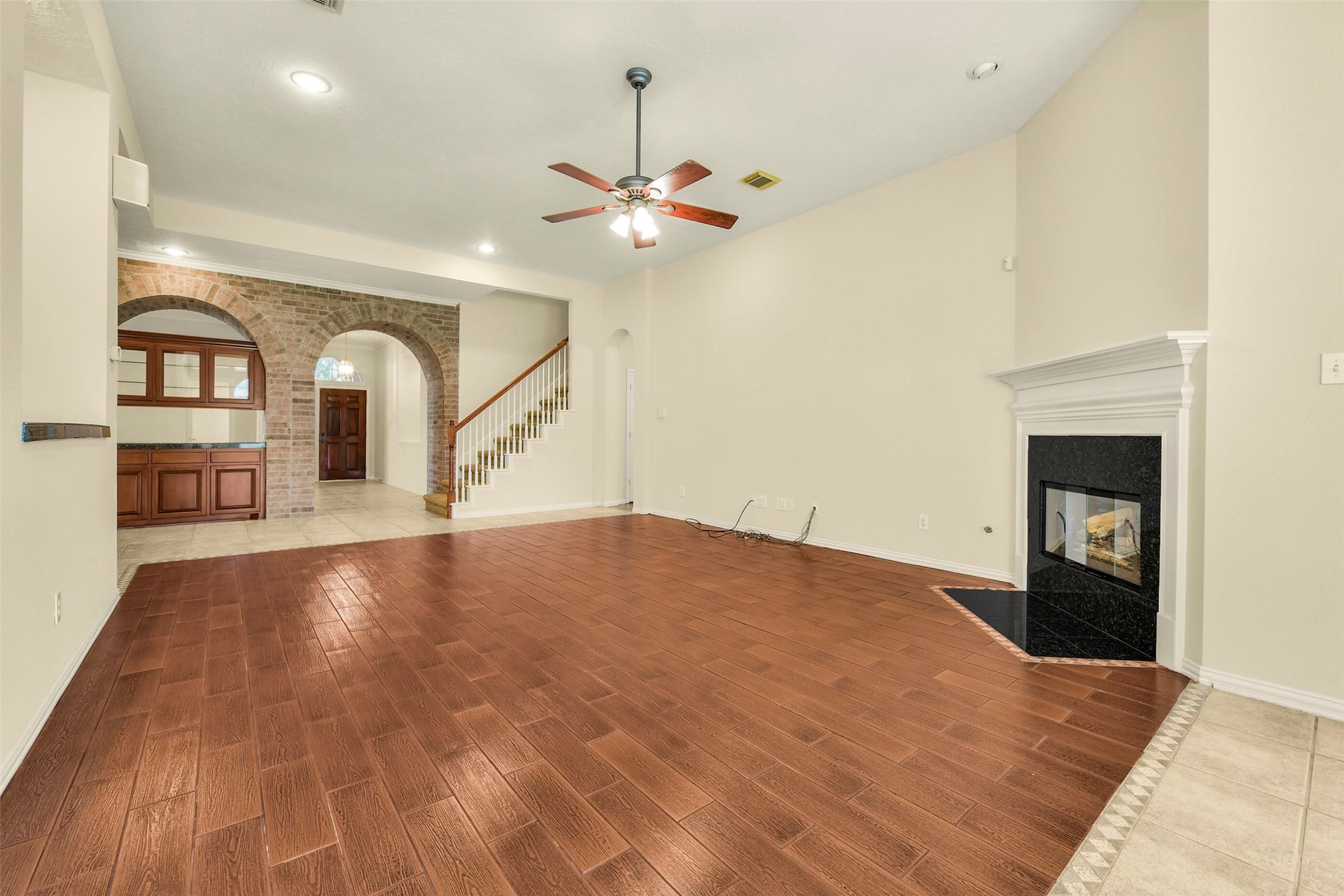 9902 Autumn Lake Trail, Pearland, TX 77584 Spacious living area featuring elegant wood-look flooring, a cozy corner fireplace, and stylish archways with exposed brick accents.