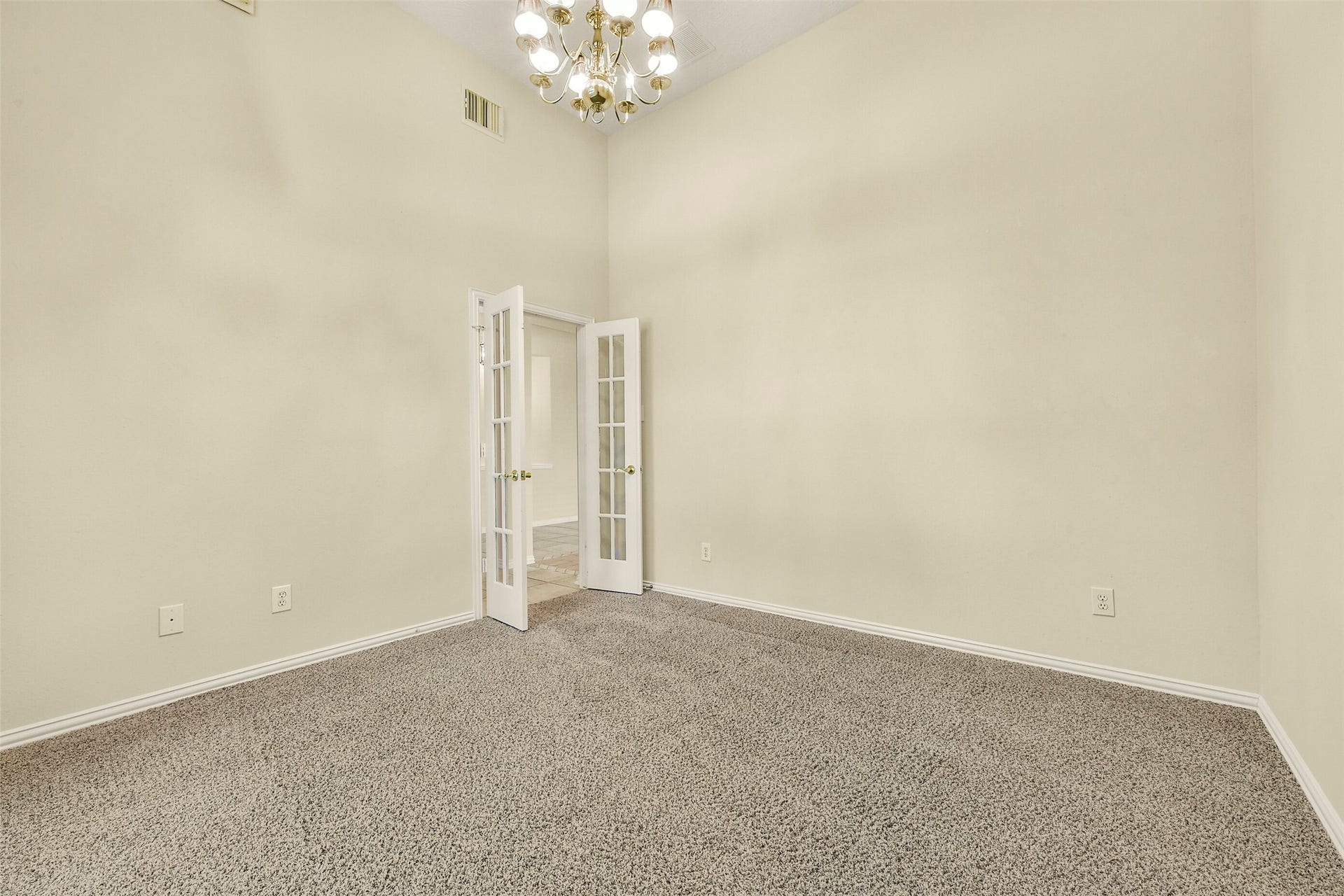 9902 Autumn Lake Trail, Pearland, TX 77584 Spacious room with plush carpeting and elegant French doors, illuminated by a stylish chandelier, perfect for an office or cozy retreat.