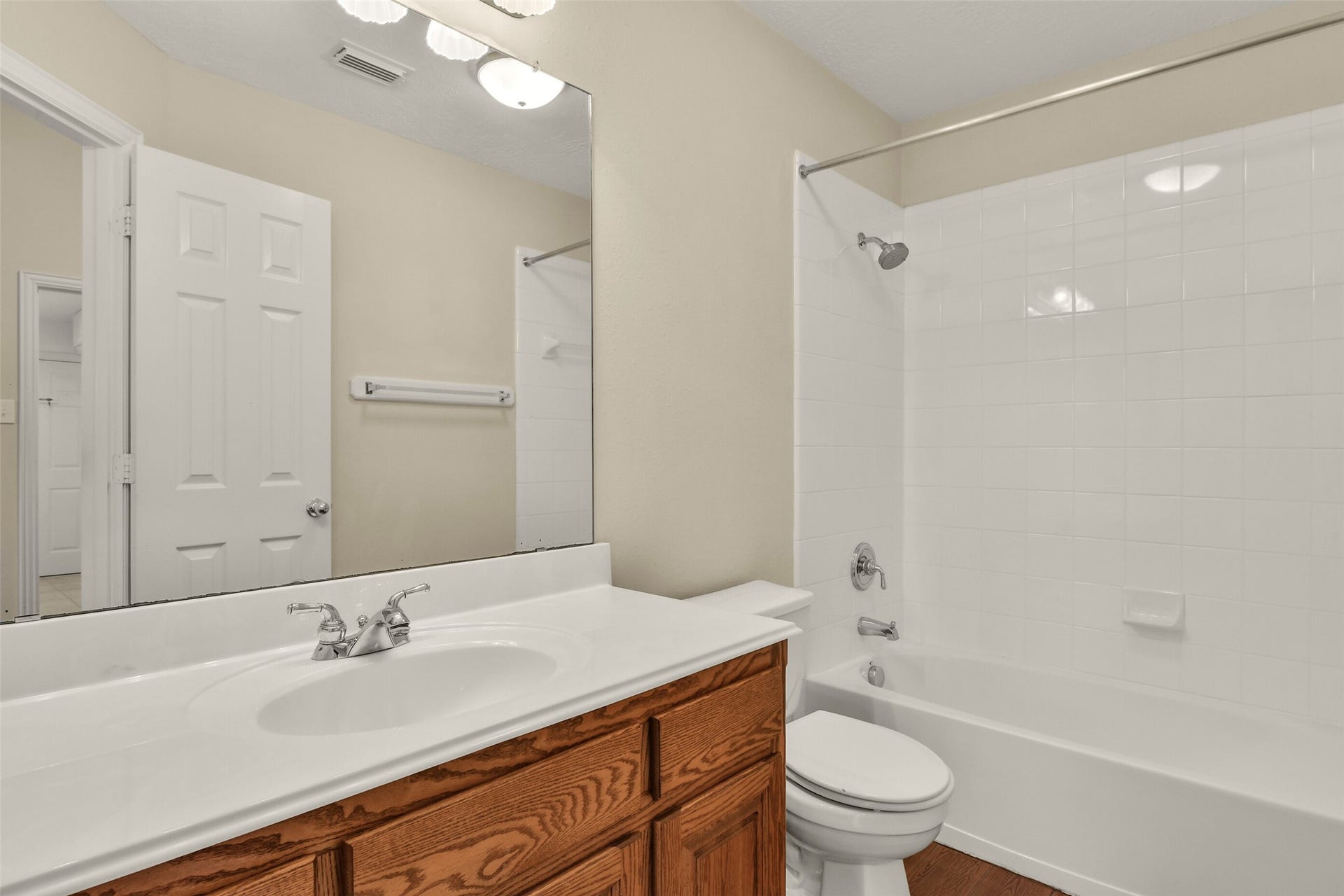 9902 Autumn Lake Trail, Pearland, TX 77584 Bright and clean bathroom featuring a classic white tiled shower-tub combo, a sleek vanity with a large mirror, and warm wood cabinetry for a welcoming touch.