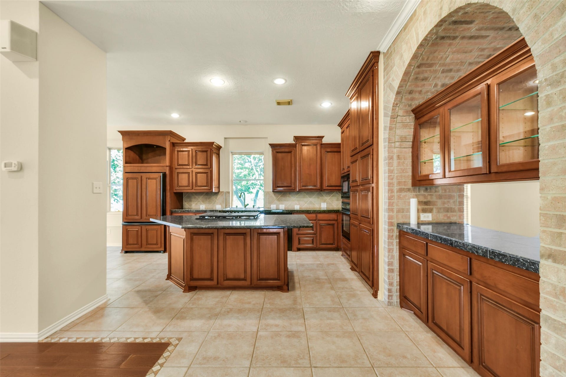 9902 Autumn Lake Trail, Pearland, TX 77584 Spacious kitchen with rich wood cabinetry and a large central island, complemented by elegant granite countertops and a charming brick archway.