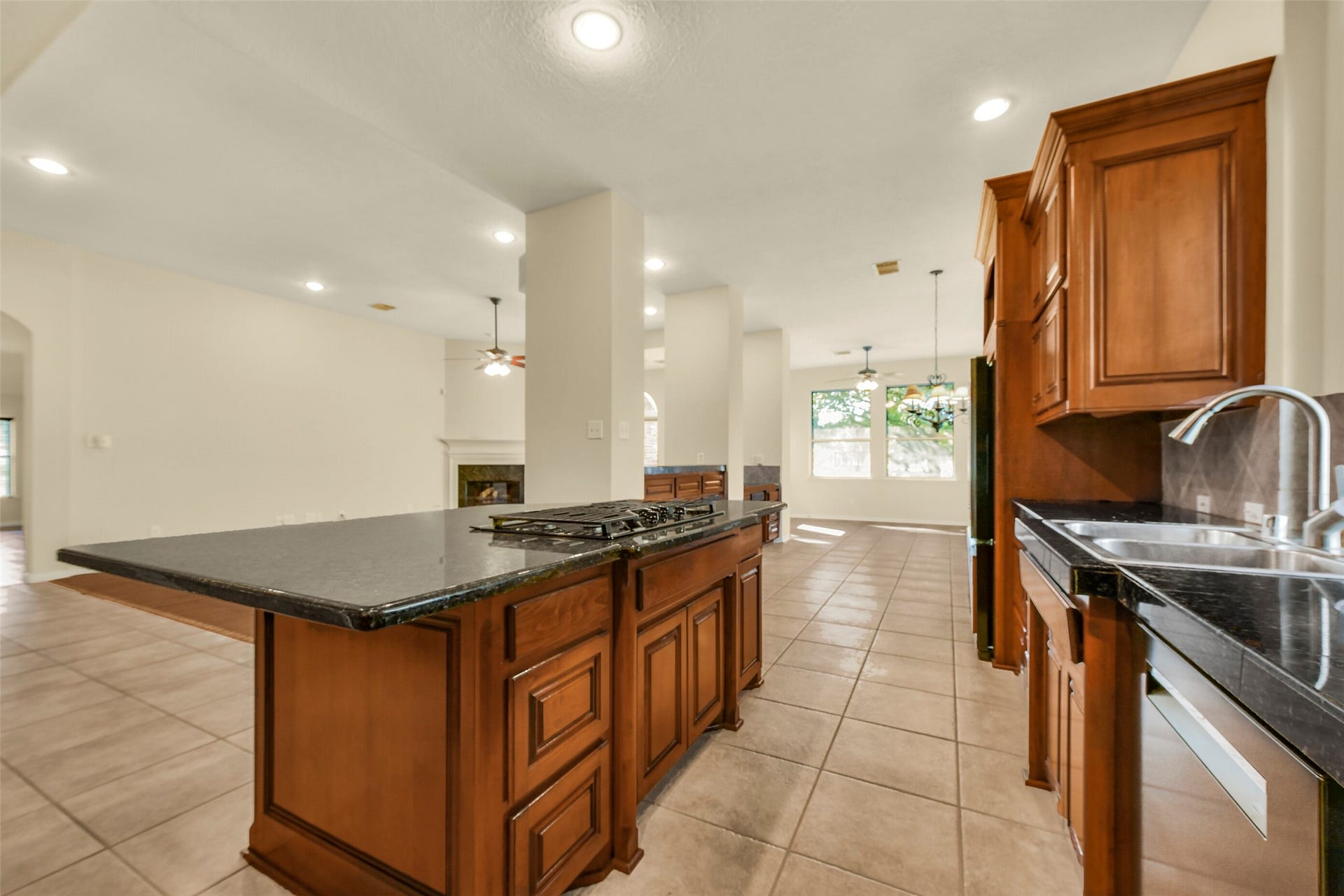 9902 Autumn Lake Trail, Pearland, TX 77584 Spacious open-concept kitchen with elegant dark countertops, rich wooden cabinetry, and a central island featuring a built-in cooktop, seamlessly flowing into a bright living area with a cozy fireplace.