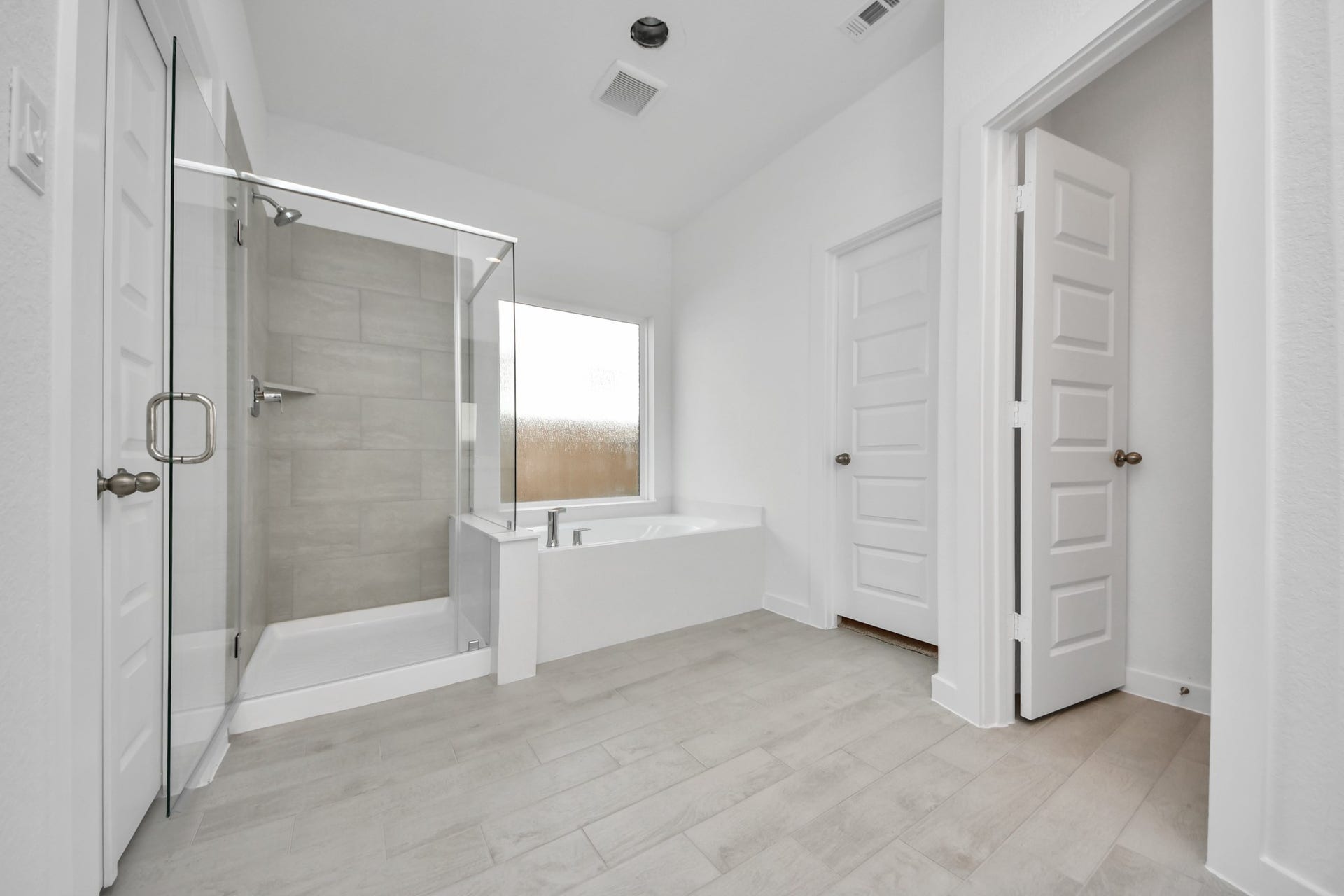 Escape to a spa-like oasis in this primary bathroom. Enjoy a walk-in shower with tile surround, a separate garden tub with custom detailing, and an elegant vanity featuring light countertops, modern hardware, and beautiful recessed lights. Experience luxury and relaxation in every detail. Sample photo of completed home with similar floor plan. Actual colors and selections may vary.