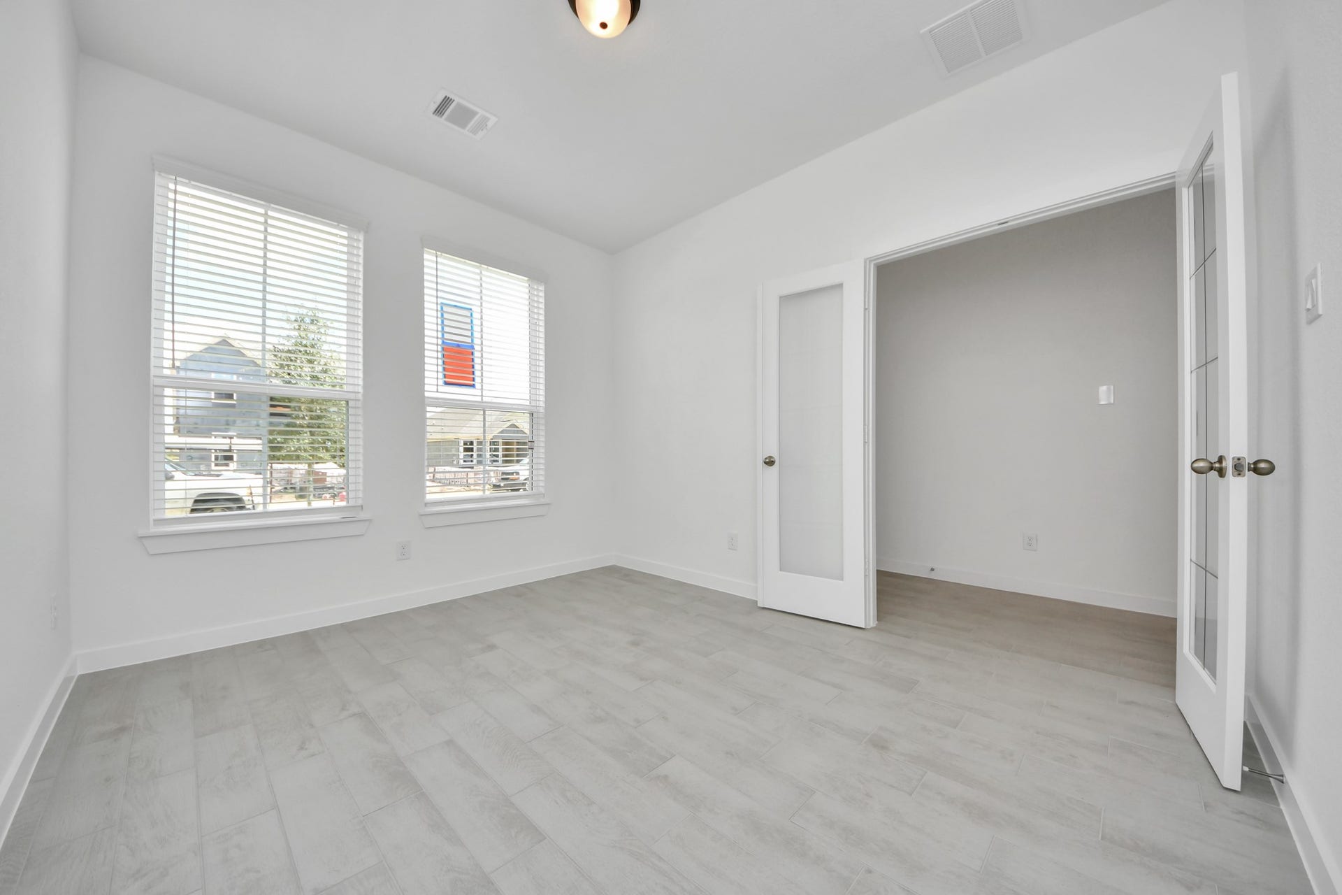 Experience the perfect blend of sophistication and warmth in this home office, boasting elegant wood-look tile flooring and flooded with natural light from expansive windows and French doors. Sample photo of completed home with similar floor plan. Actual colors and selections may vary.