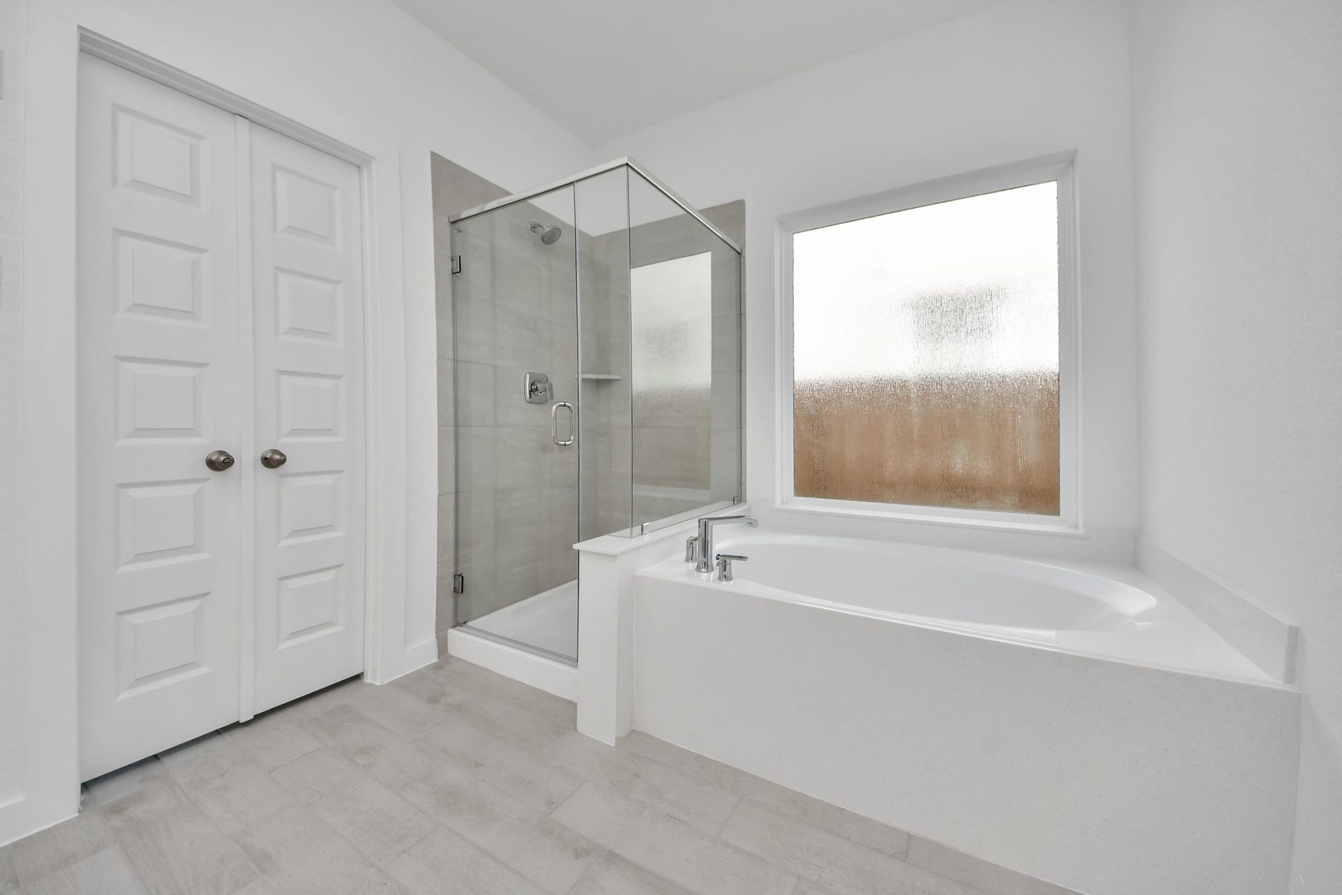 Indulge in a spa-like retreat within the confines of this primary bathroom. Delight in a spacious walk-in shower enveloped in stylish tile surround, unwind in a separate garden tub adorned with custom detailing. Sample photo of completed home with similar floor plan. Actual colors and selections may vary.