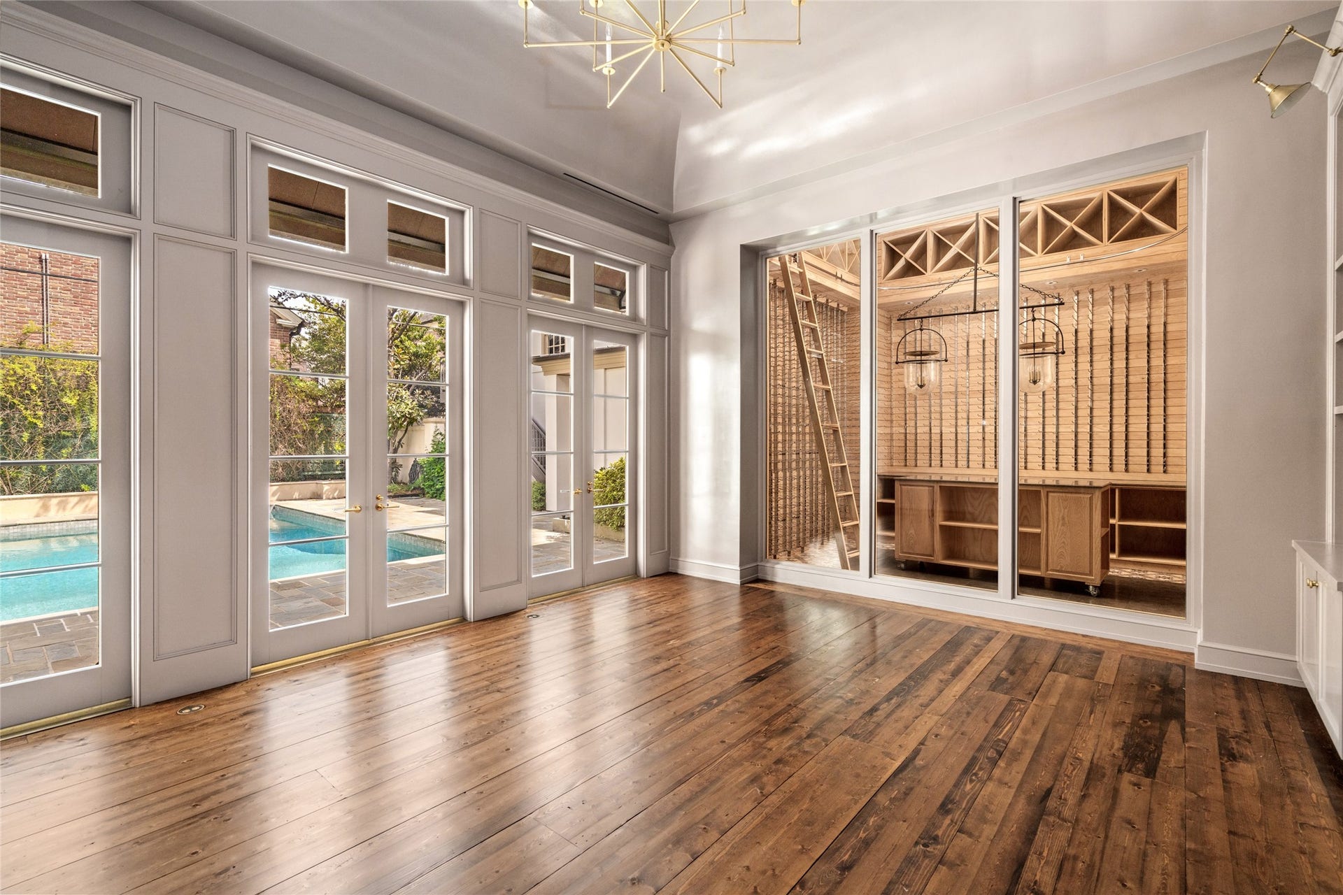 Home office with French doors overlooking the pool and a glass wall showcasing the adjoining wine room.