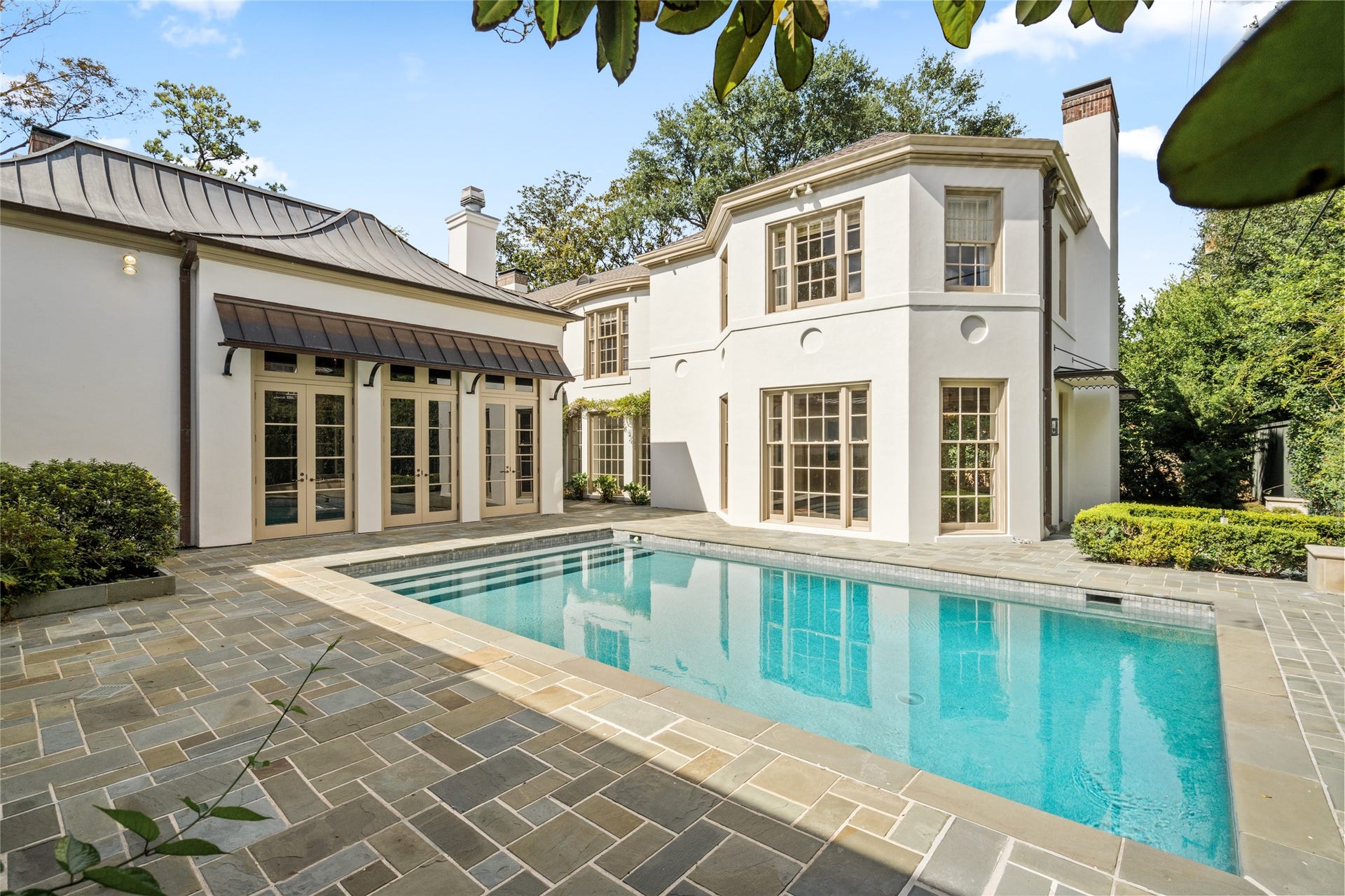 Pool courtyard with spacious stone terrace, french doors, and landscaped surroundings-ideal for outdoor entertaining.