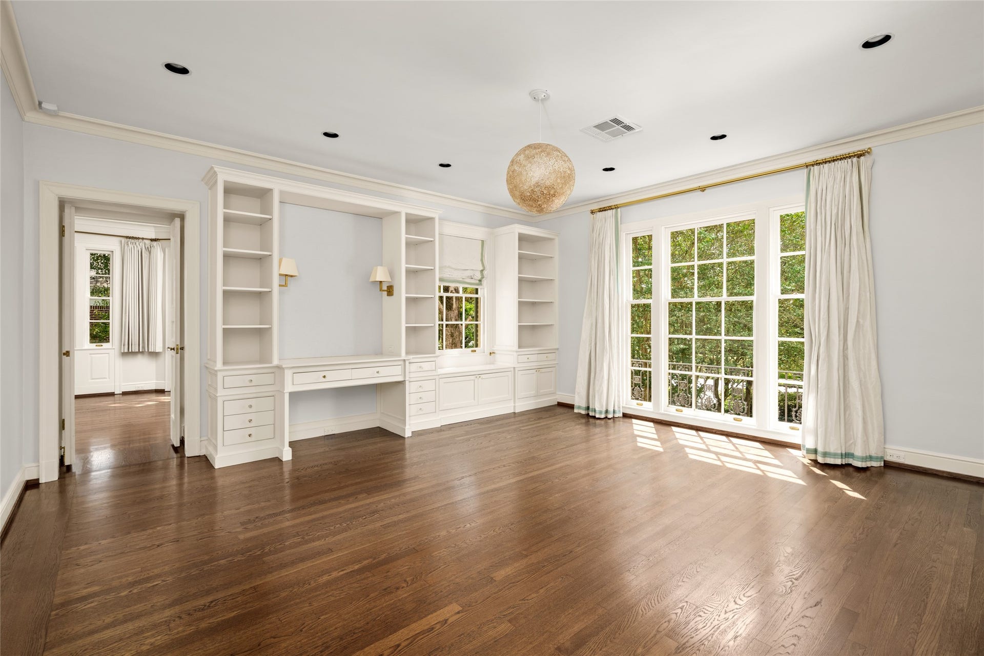 Spacious bedroom with built in shelving and desk tall windows overlooking the front grounds showing access to the adjoining sun room
