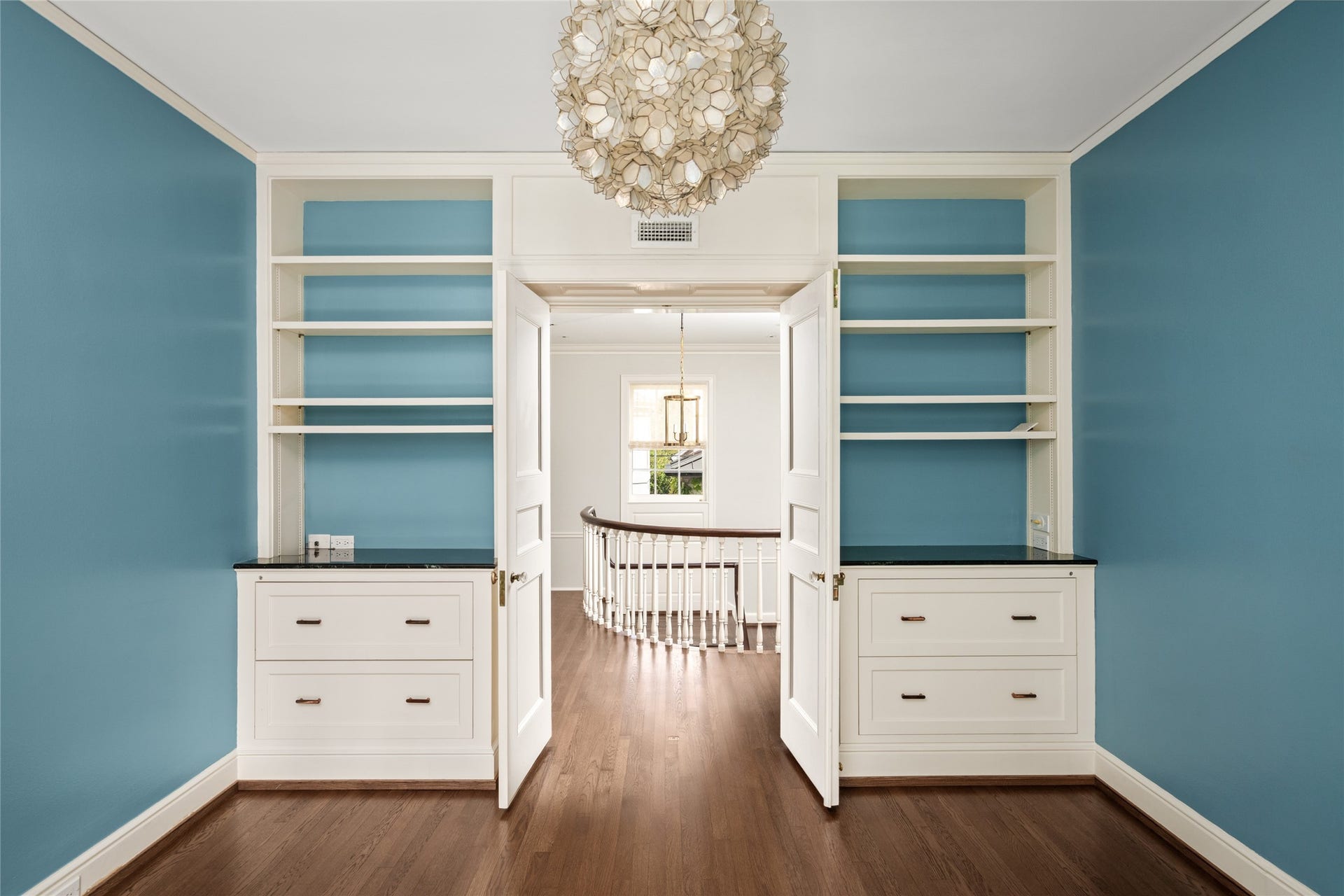 Bright and inviting room featuring elegant built-in shelving, rich hardwood floors, and a stunning modern chandelier, perfect for a stylish home office or library.