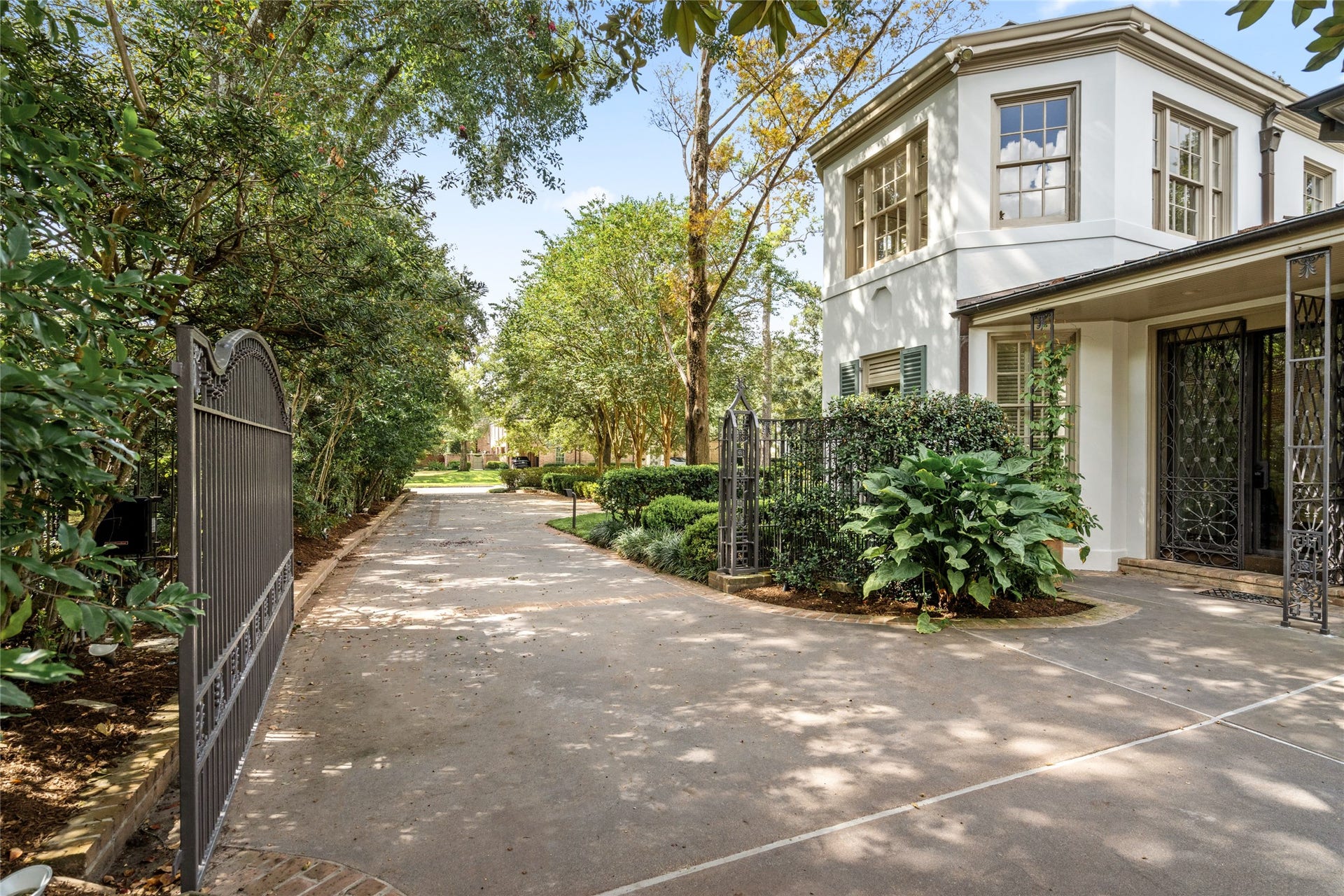 Long driveway gated by decorative wrought-iron fencing and lush landscape beside the covered side entrance.
