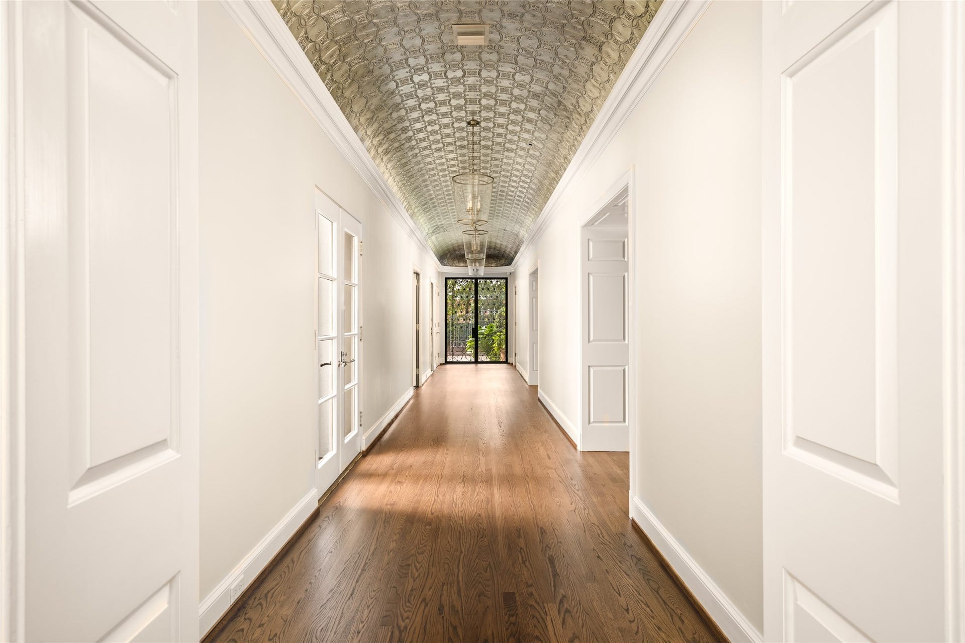 Elegant hallway with rich hardwood floors, ornate ceiling detailing, and ample natural light from multiple doorways.