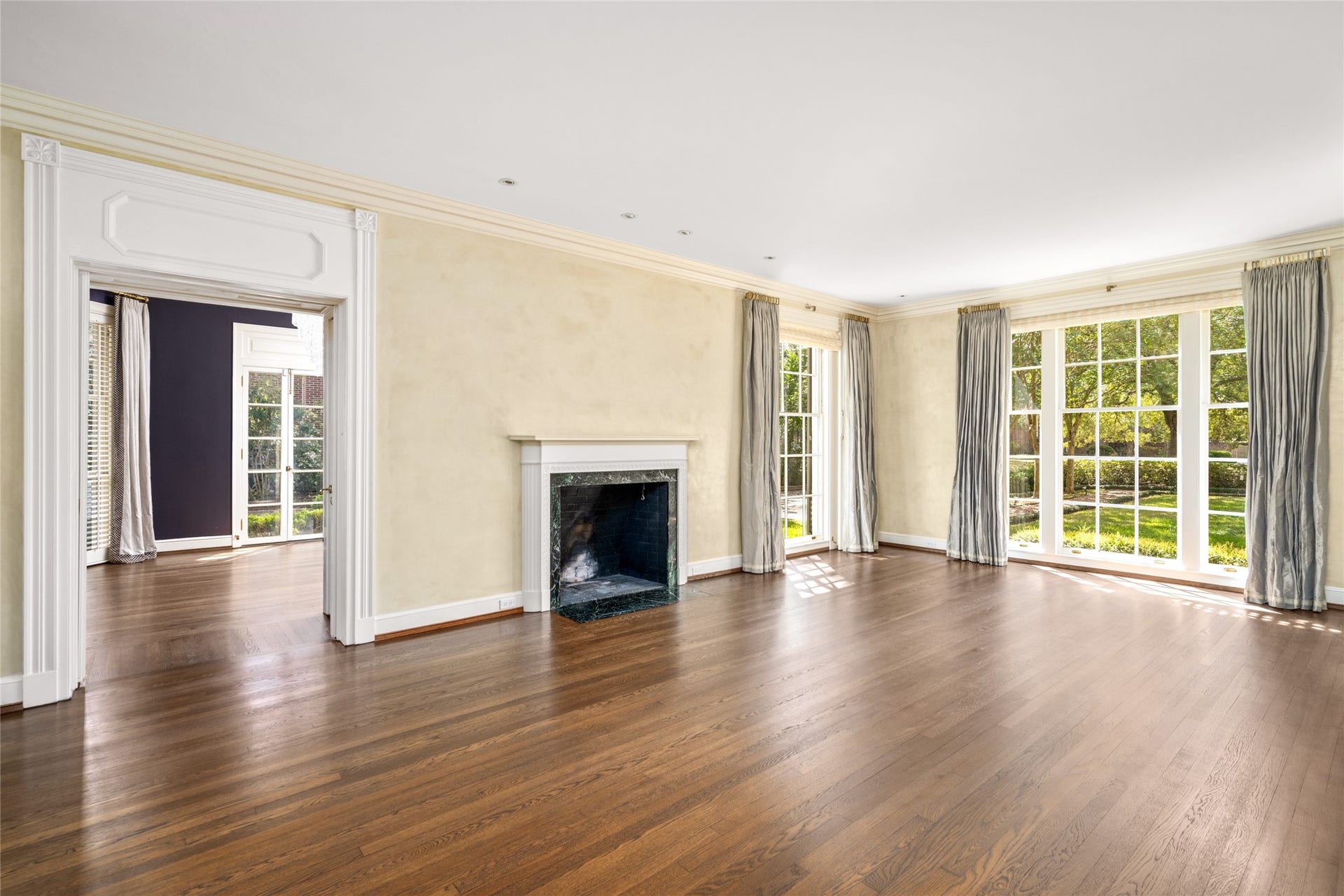 Spacious living room with a classic fireplace, large windows overlooking the grounds, and access to the adjoining sun room.