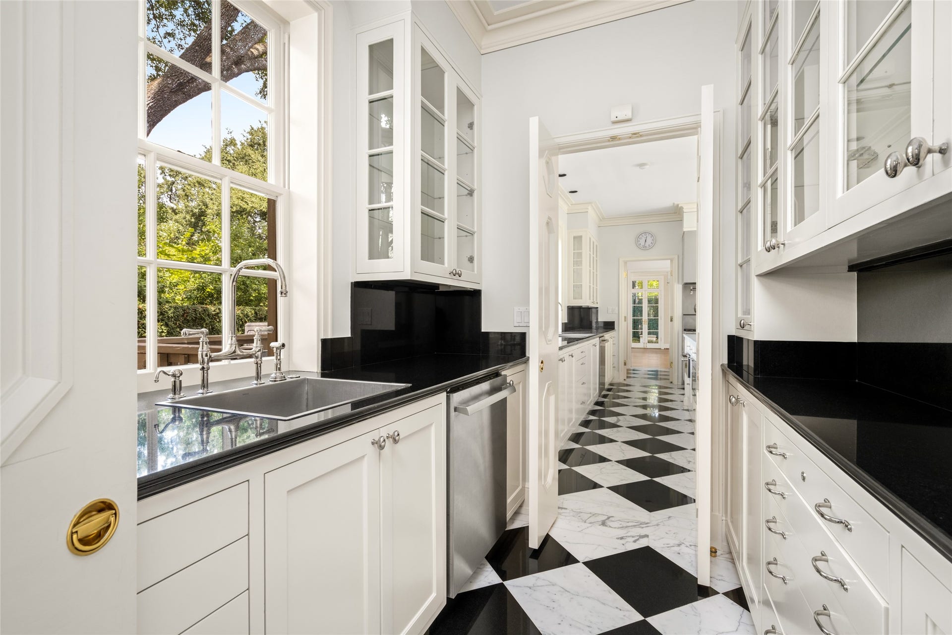 Charming butlers pantry featuring sleek black countertops, a classic black-and-white checkered floor, and ample cabinetry with glass fronts, all bathed in natural light from large windows.
