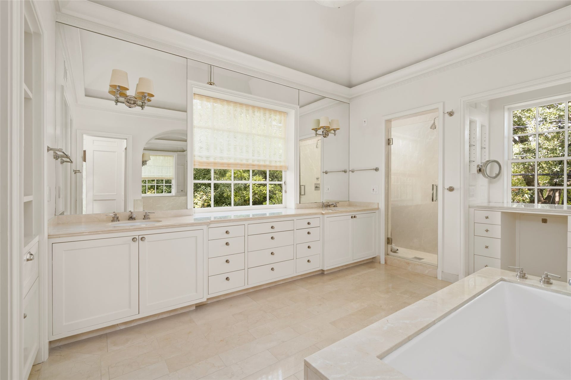 Primary bath with white marble finishes, dual sinks, a soaking tub, separate shower, and built in vanity.