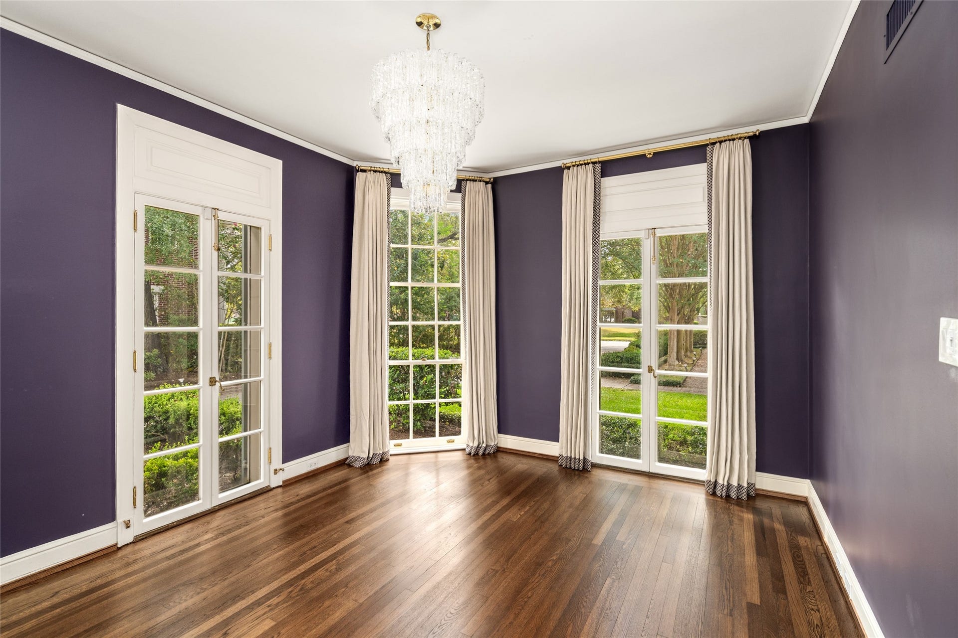 Sitting room with rich purple walls, crystal chandelier and tall windows and french doors framing garden views.