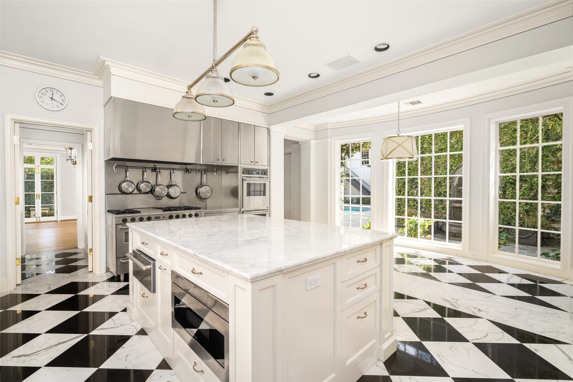 Light-filled kitchen featuring spacious center island, crisp white cabinetry, professional-style range, and straiking black and white checkerboard floors.