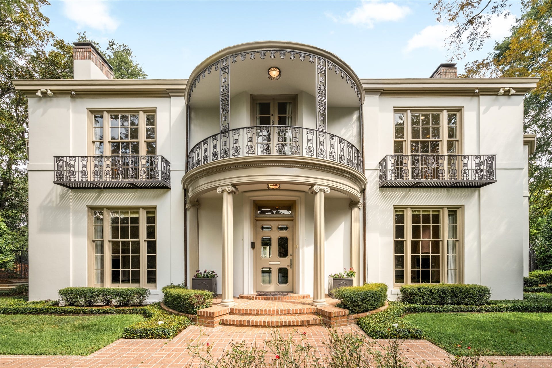 Closer view of the estate's facade, highlighting decorative iron balconies, a curved portico and classic columns.