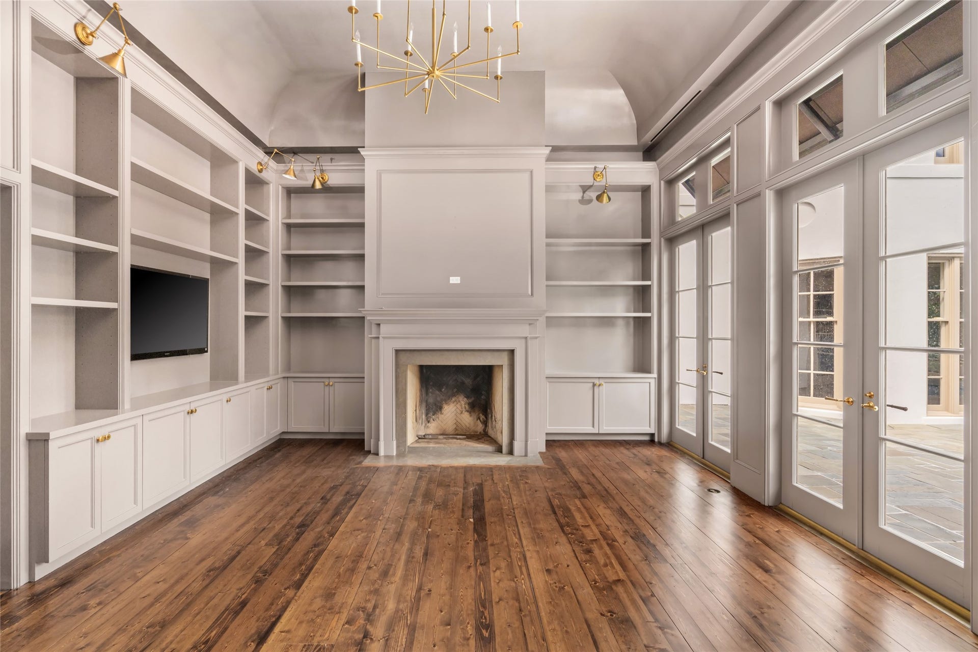 Study/Home office featuring extensive built-in shelving and cabinetry, a classic fireplace.  Glass paneled French doors and transom windows fill the room with natural light and open up to the pool.