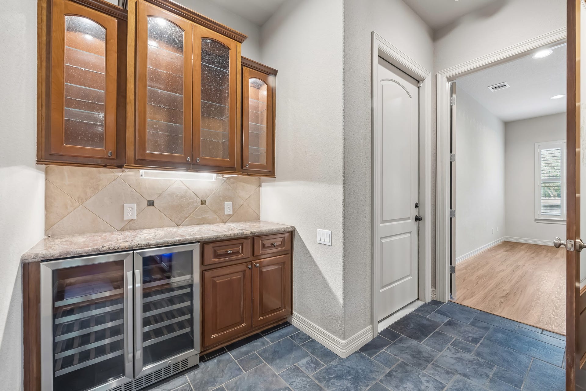 Elegant butler's pantry with rich wood cabinetry, glass display doors, and a wine fridge.